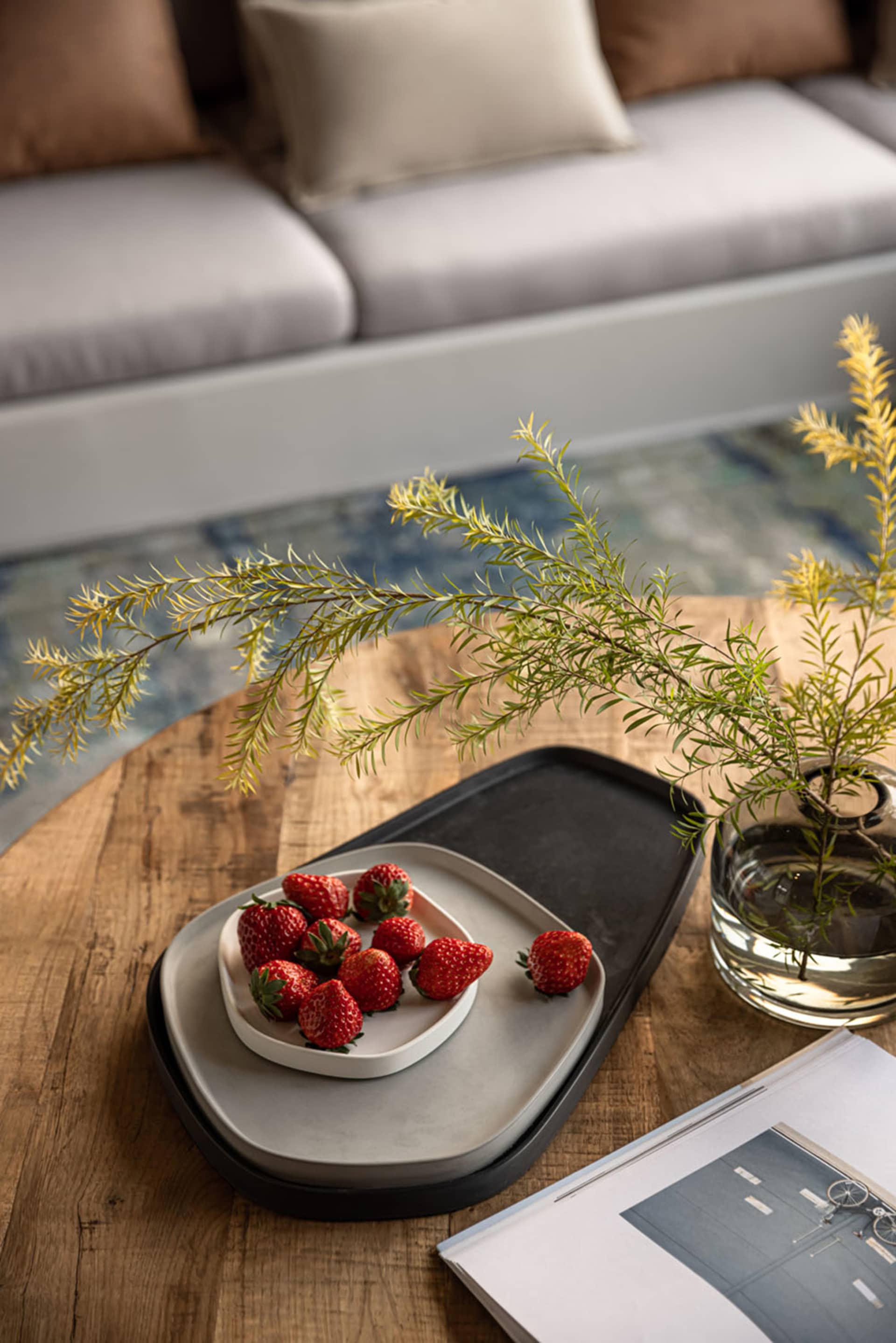 A modern minimalist living room featuring wooden furniture and fresh strawberries on a tray.