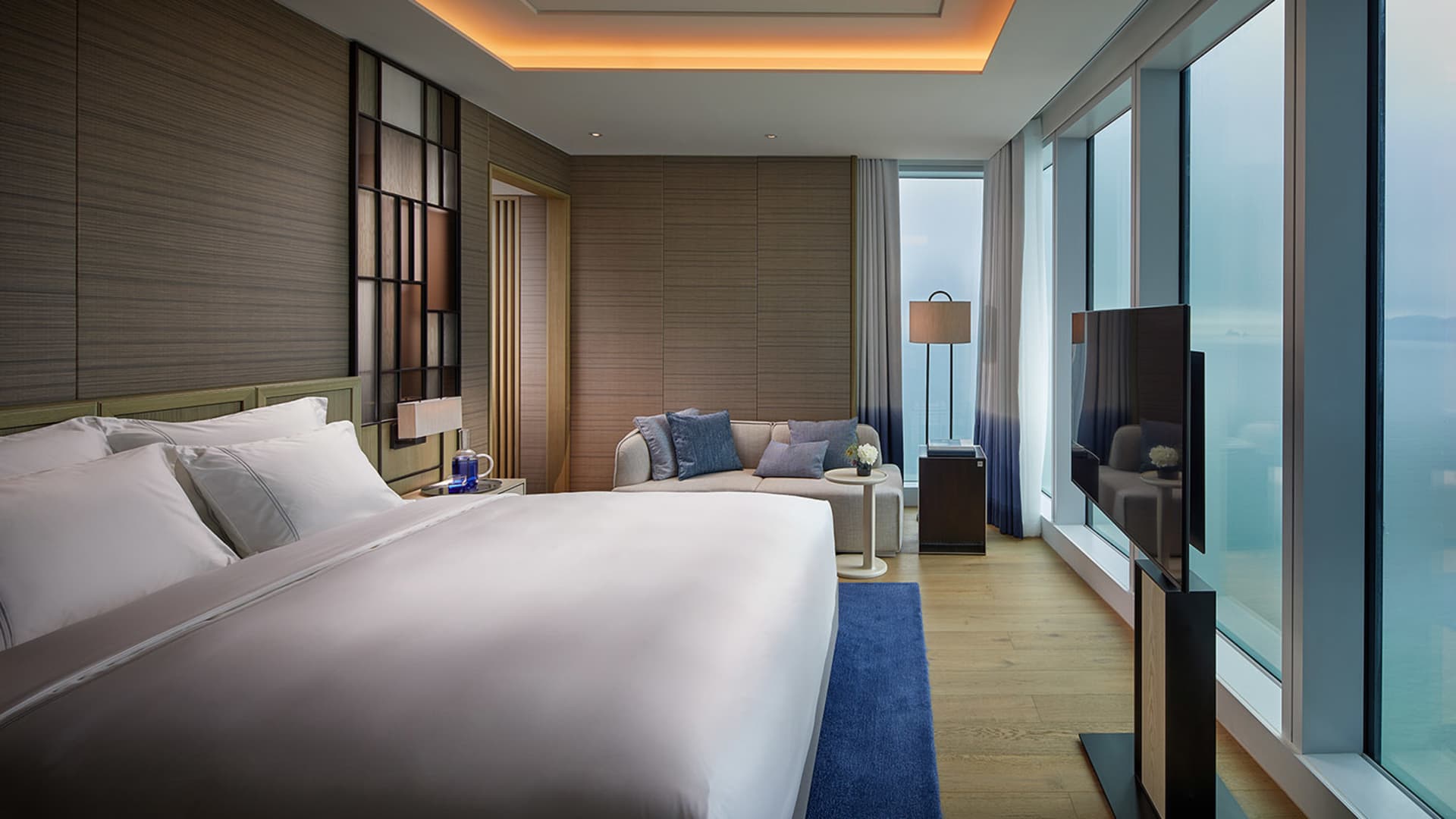 A modern residential suite with minimalist design, featuring wood, glass, and fabric materials.