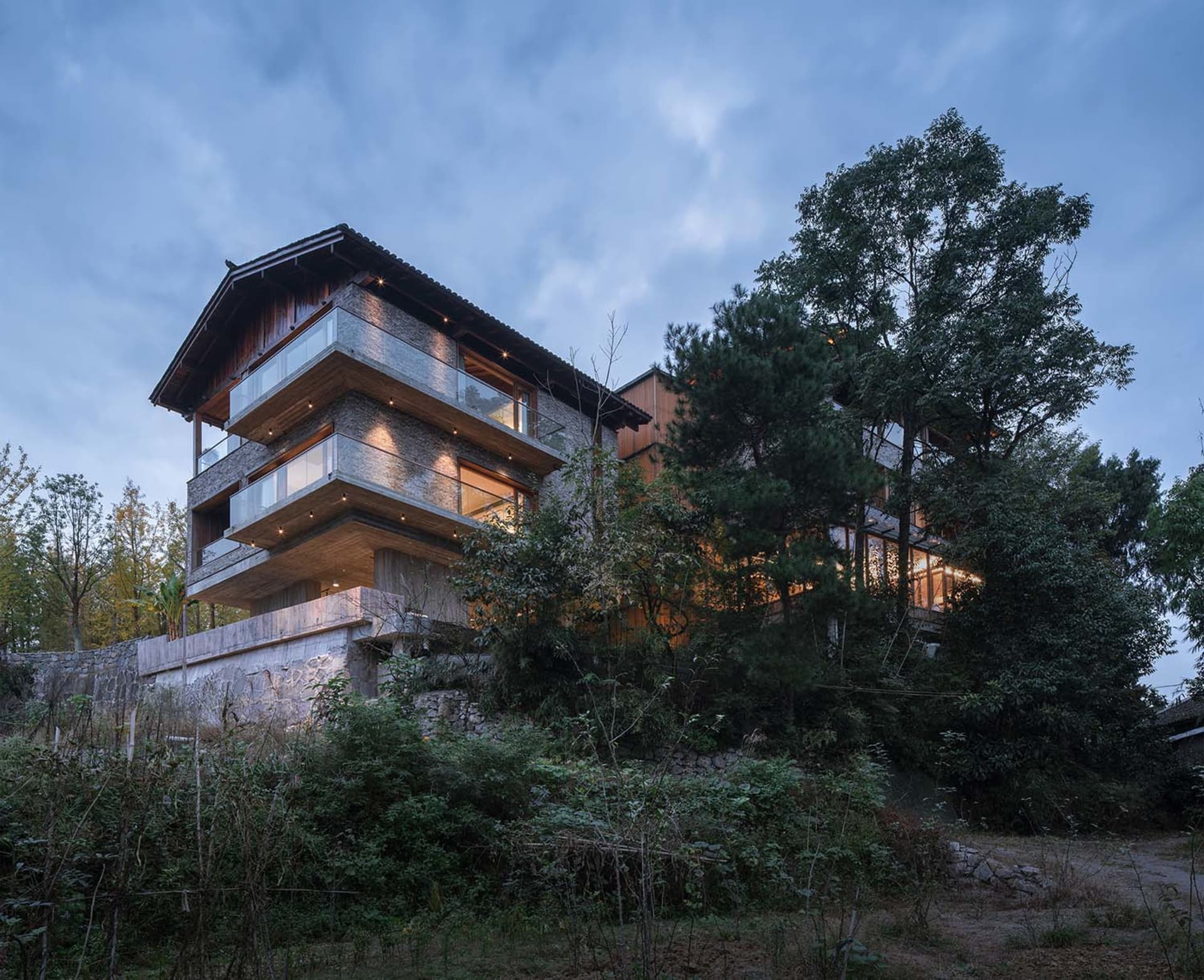 現代住宅建築外觀採用石材與木質元素,黃昏時分燈光點亮。