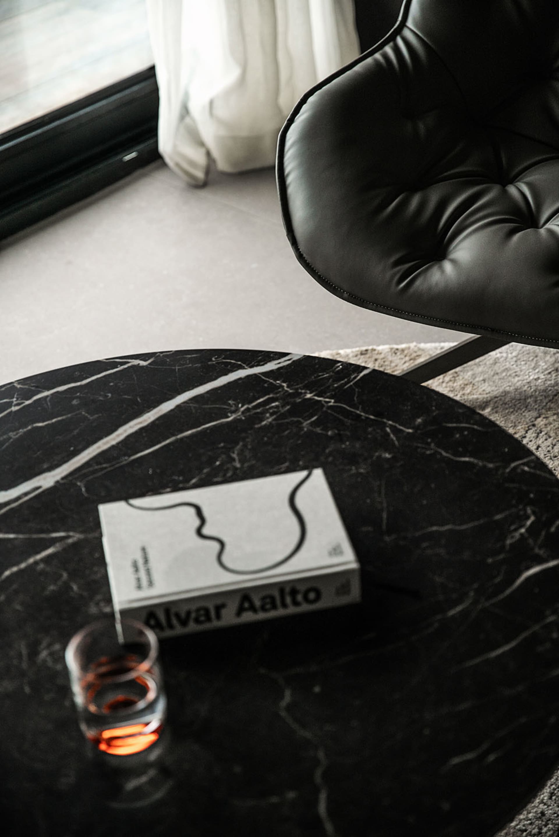 A marble coffee table with a book titled 'Alvar Aalto' and a glass of drink.