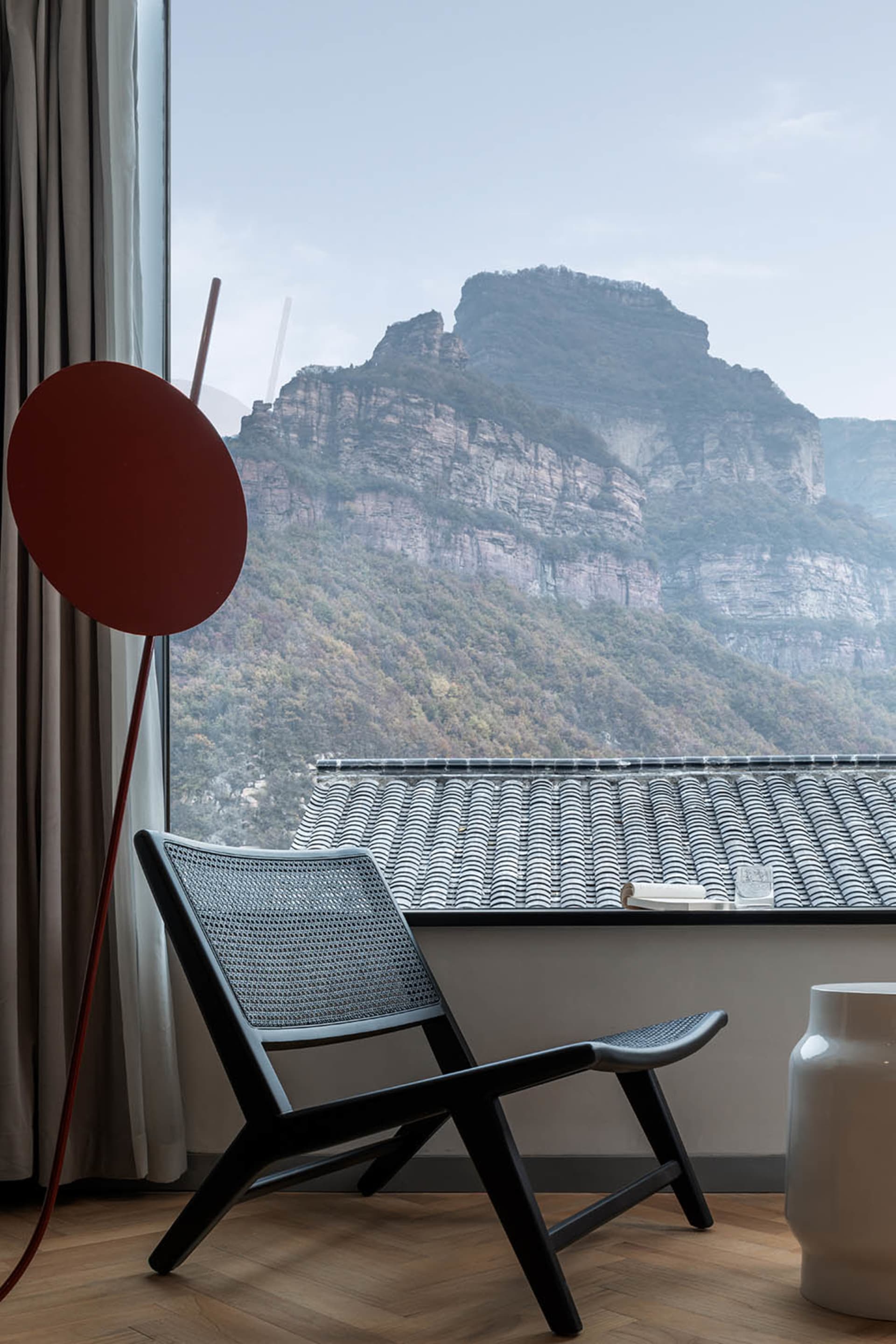 現代室內擺放紅色圓形物件於木質地板上，窗外可見山景。