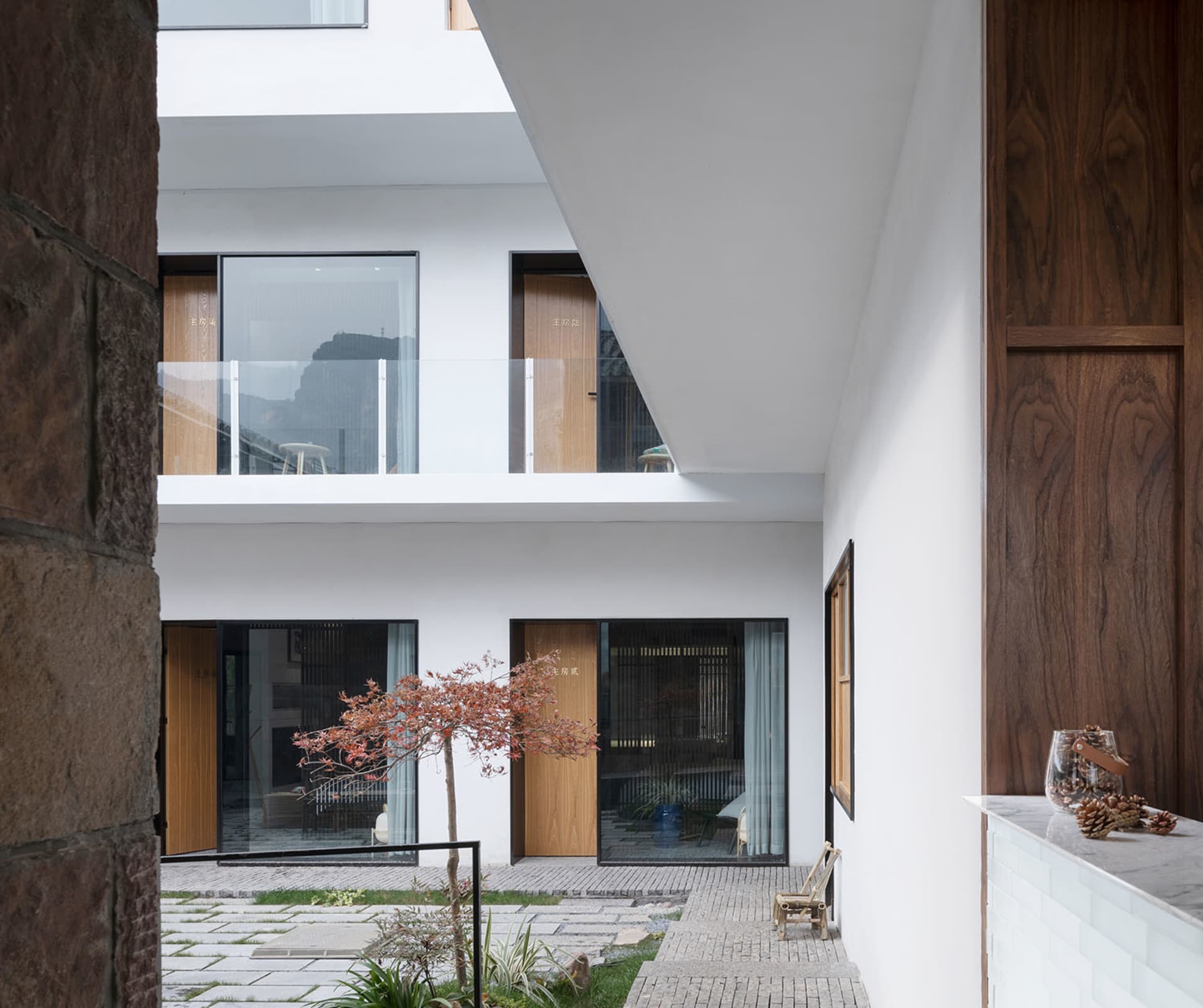 A modern residential courtyard with white walls and wooden doors, featuring glass windows and a tree in the center.