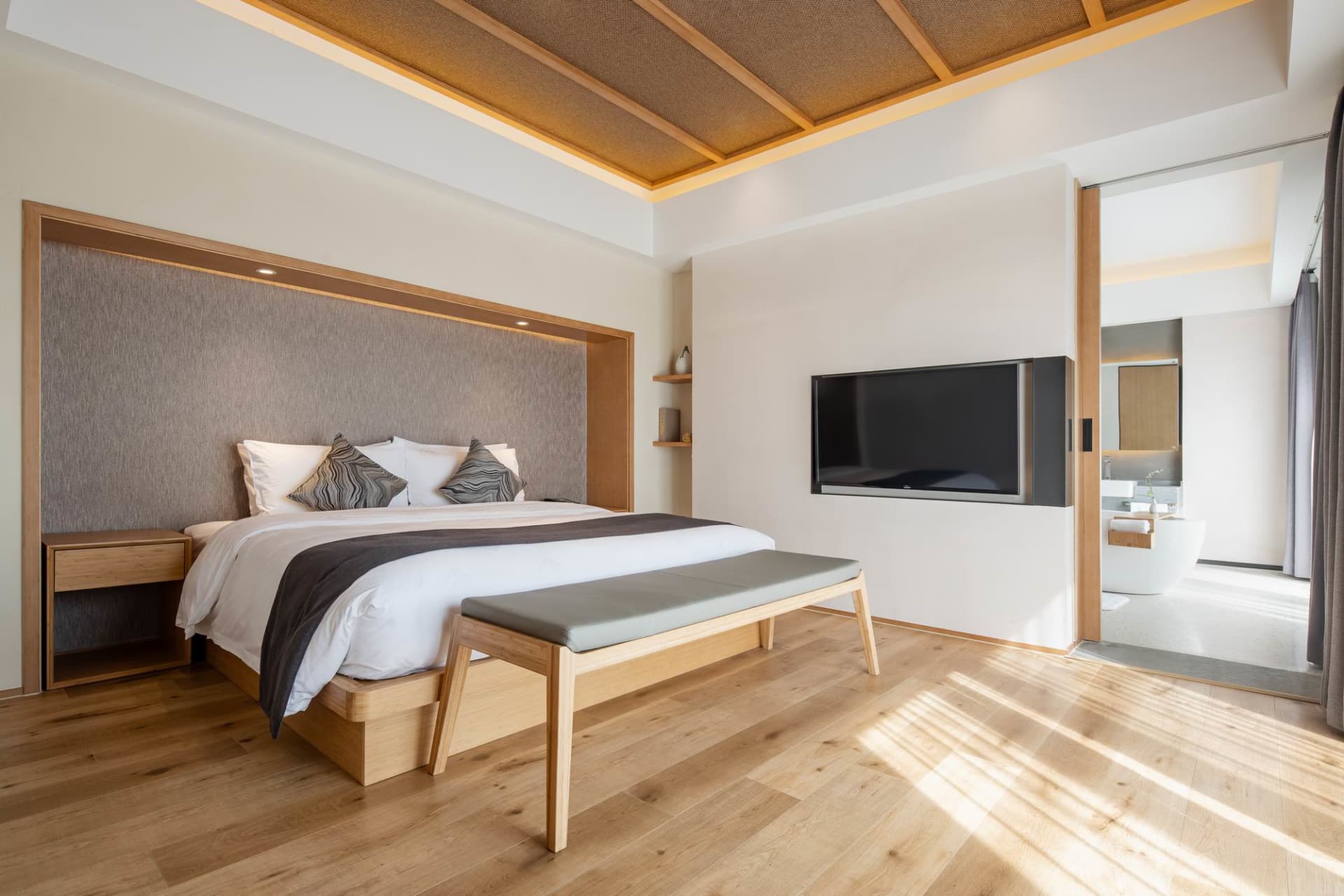 A minimalist bedroom with wooden furniture, a large bed, and a mounted television.