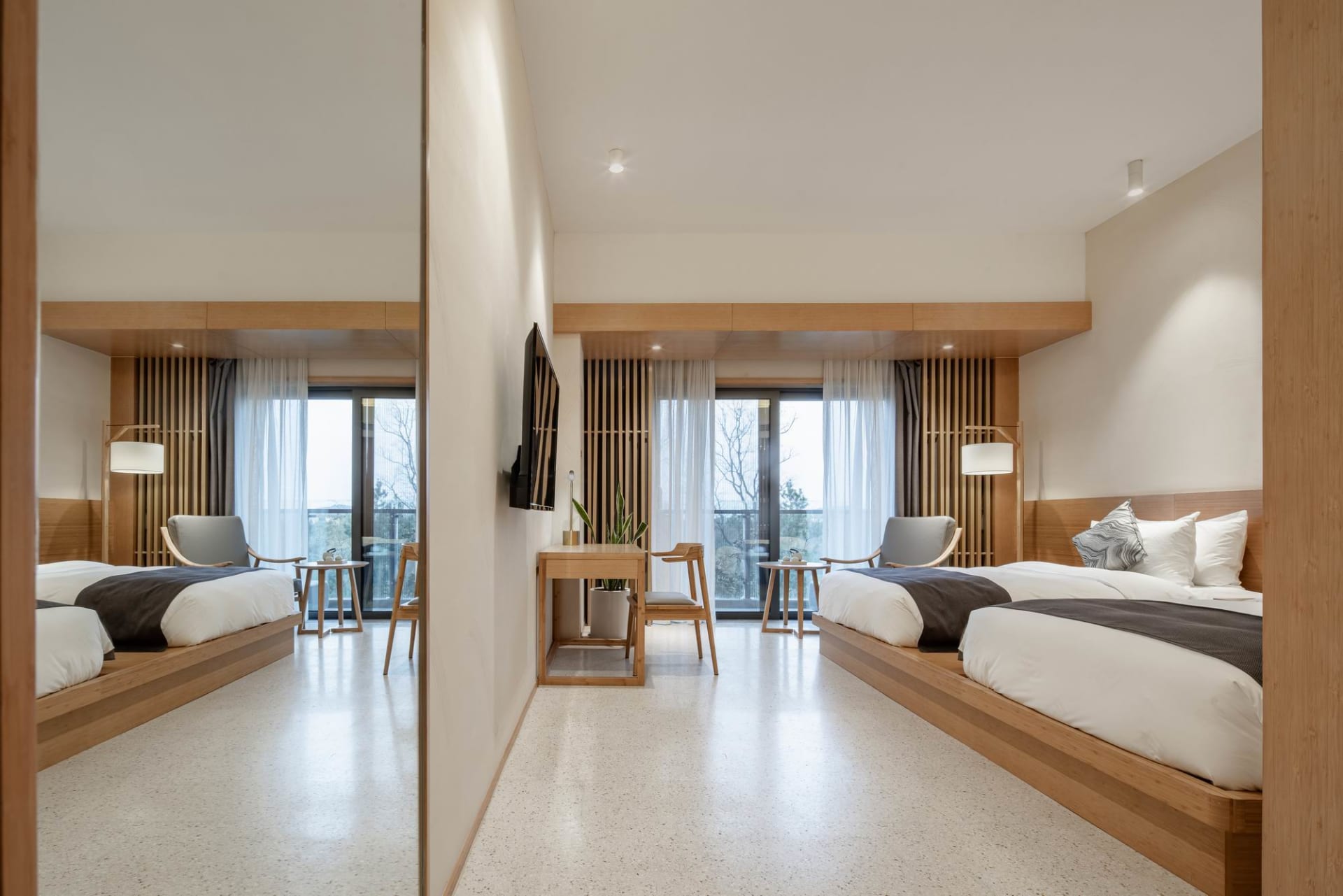 Modern minimalist bedroom featuring wooden furniture and white bedding, with a large window and balcony.