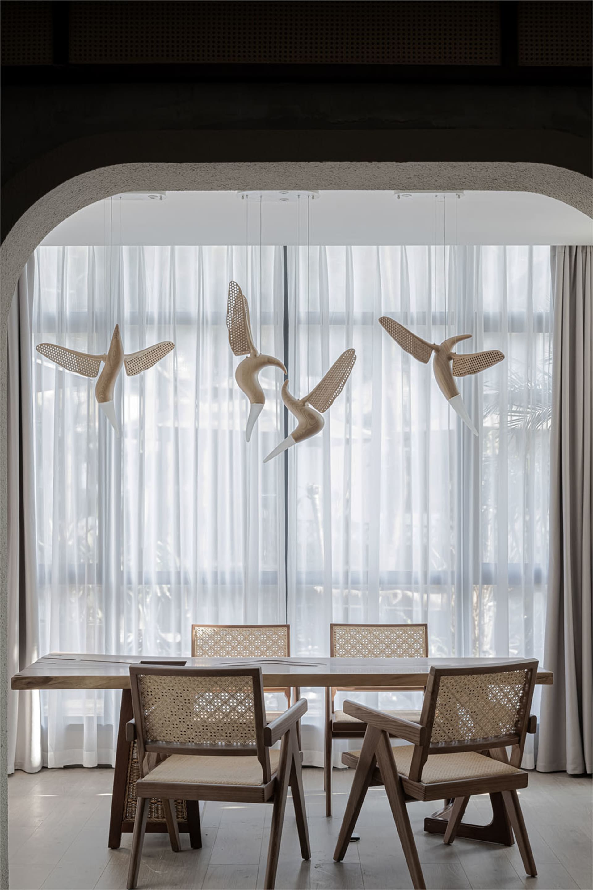 Modern dining room with wooden table and chairs, adorned with wooden bird sculptures hanging from the ceiling, set against sh