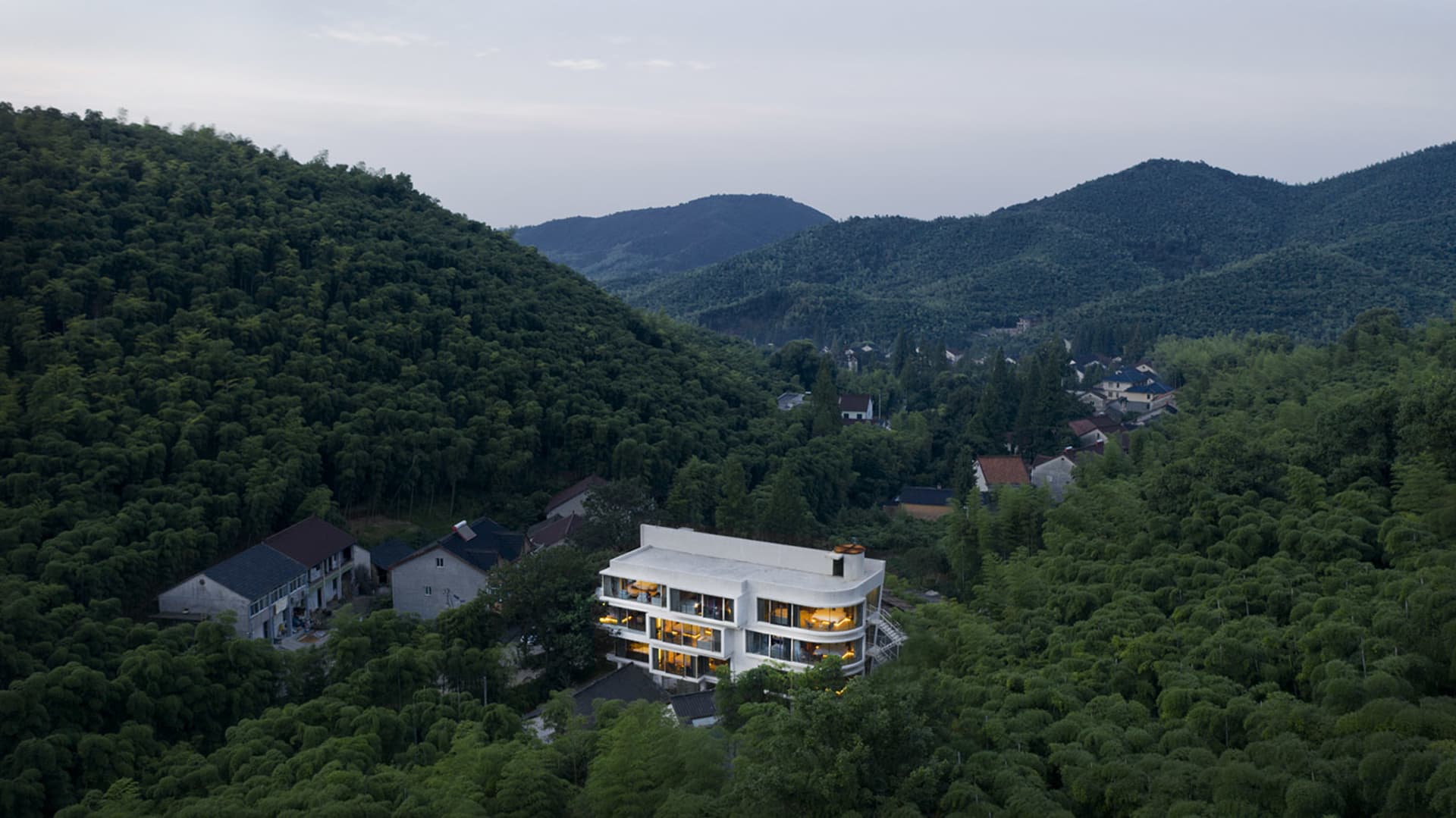 一棟現代白色住宅坐落於綠意盎然的森林山坡上。