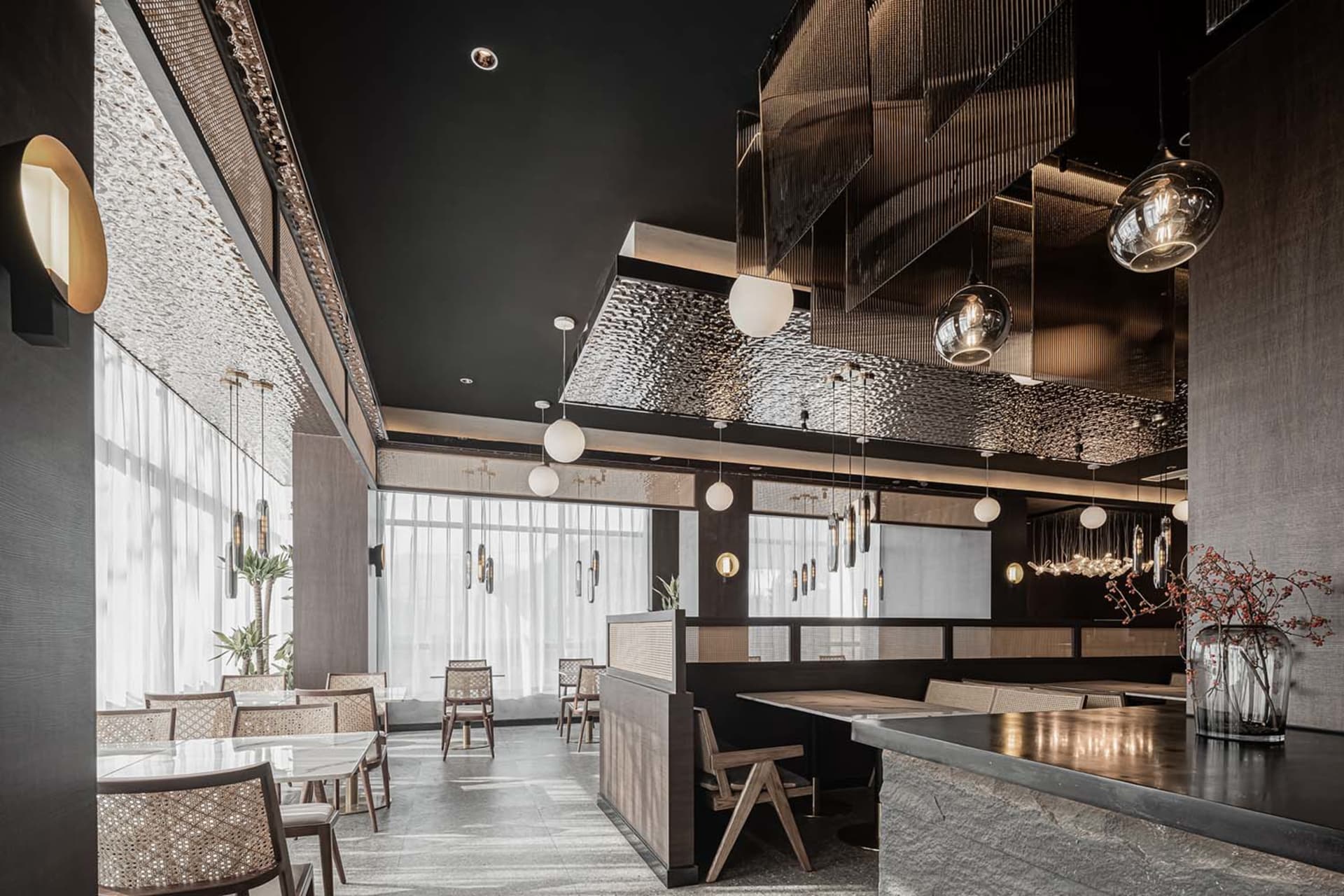 A modern restaurant interior featuring a textured metallic ceiling and glass chandelier fixtures.