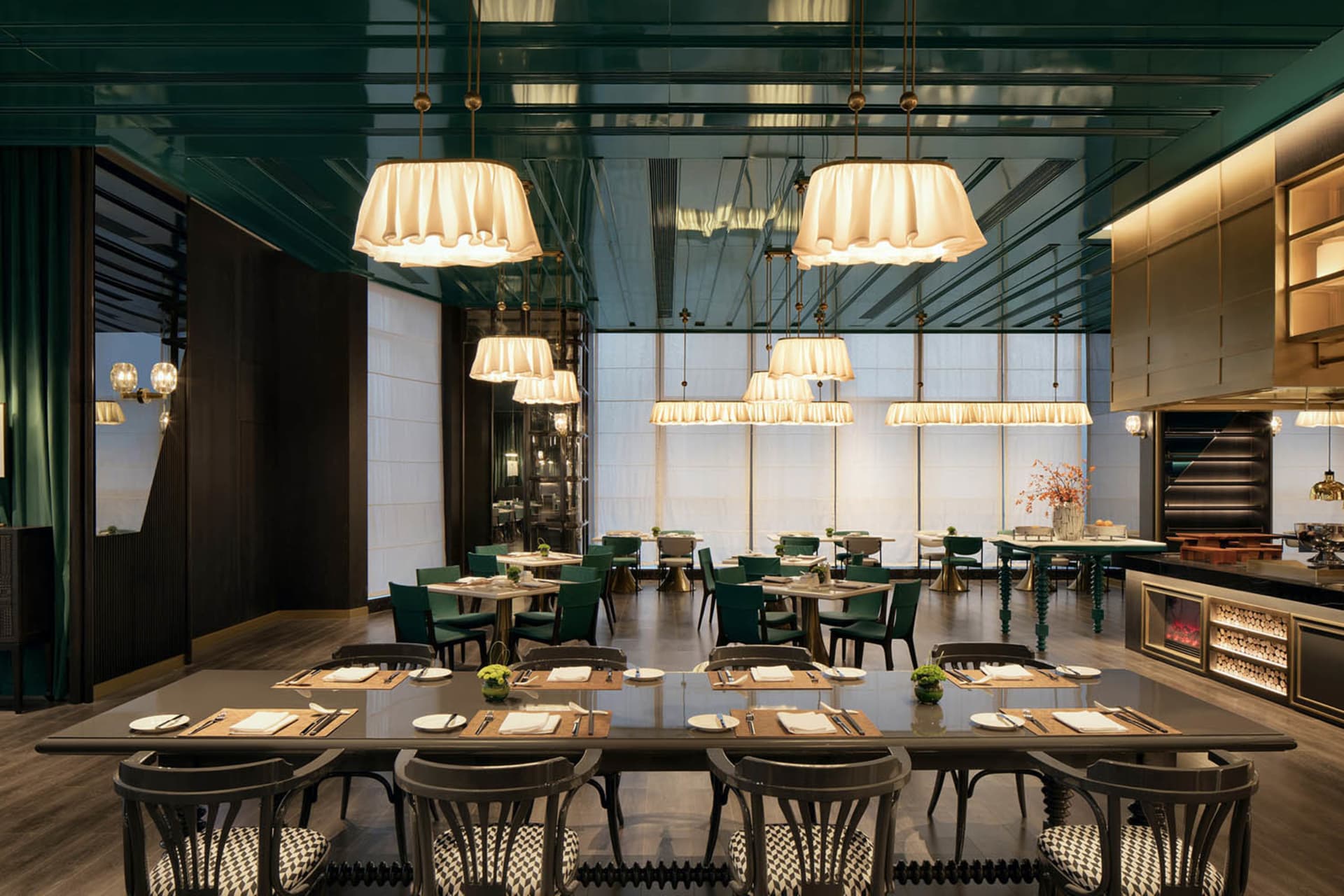 A modern restaurant dining room with large windows, green pendant lights, and meticulously set tables.