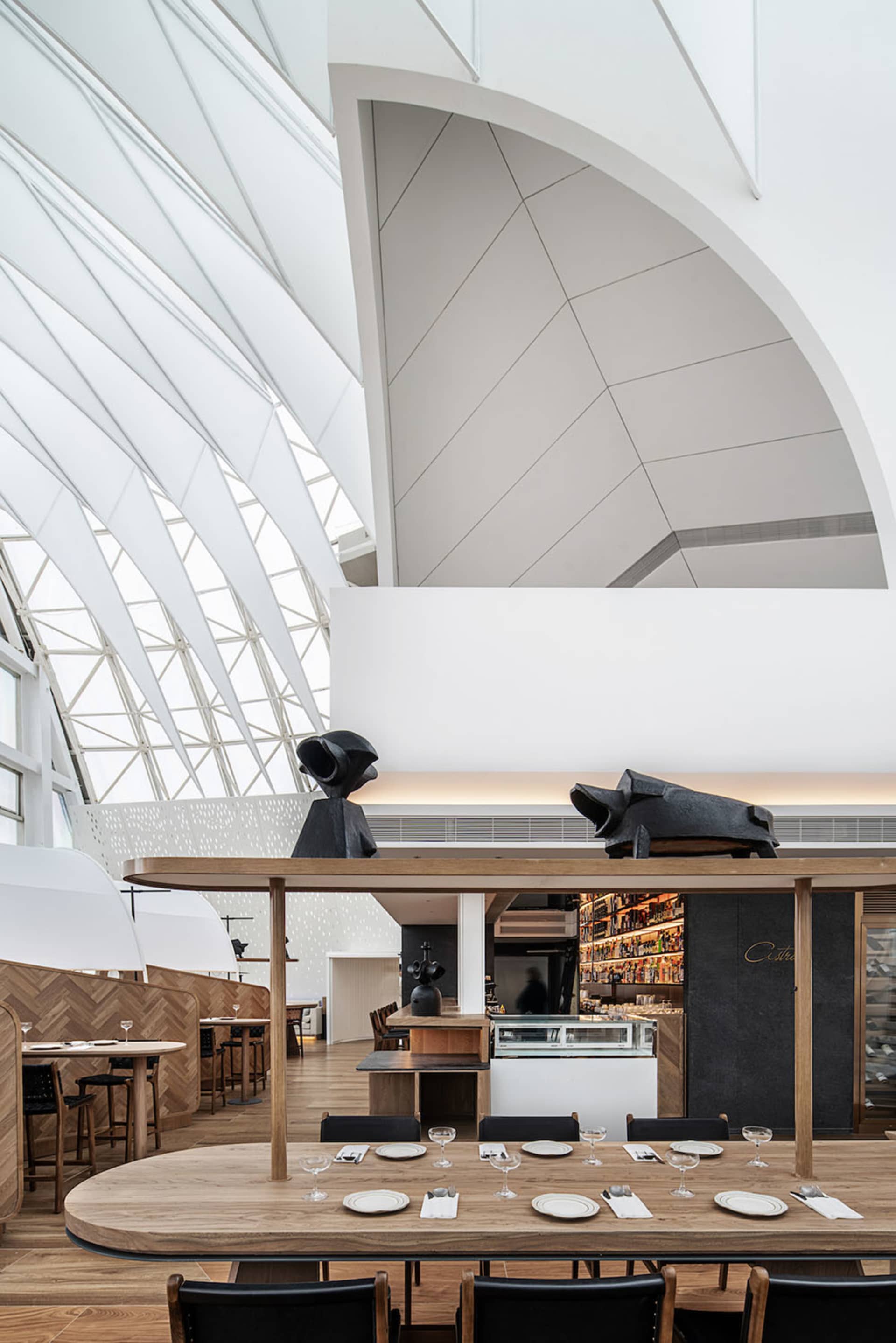 Modern restaurant interior with white walls, wood tables, concrete floor, and metal accents.