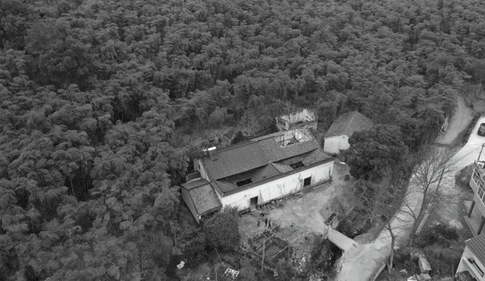 Aerial view of a rural farm house surrounded by dense forest with concrete walls.