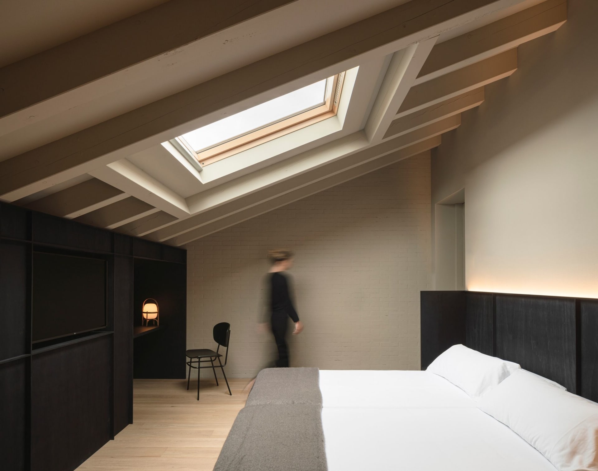 Minimalist bedroom with wooden furniture and a skylight.