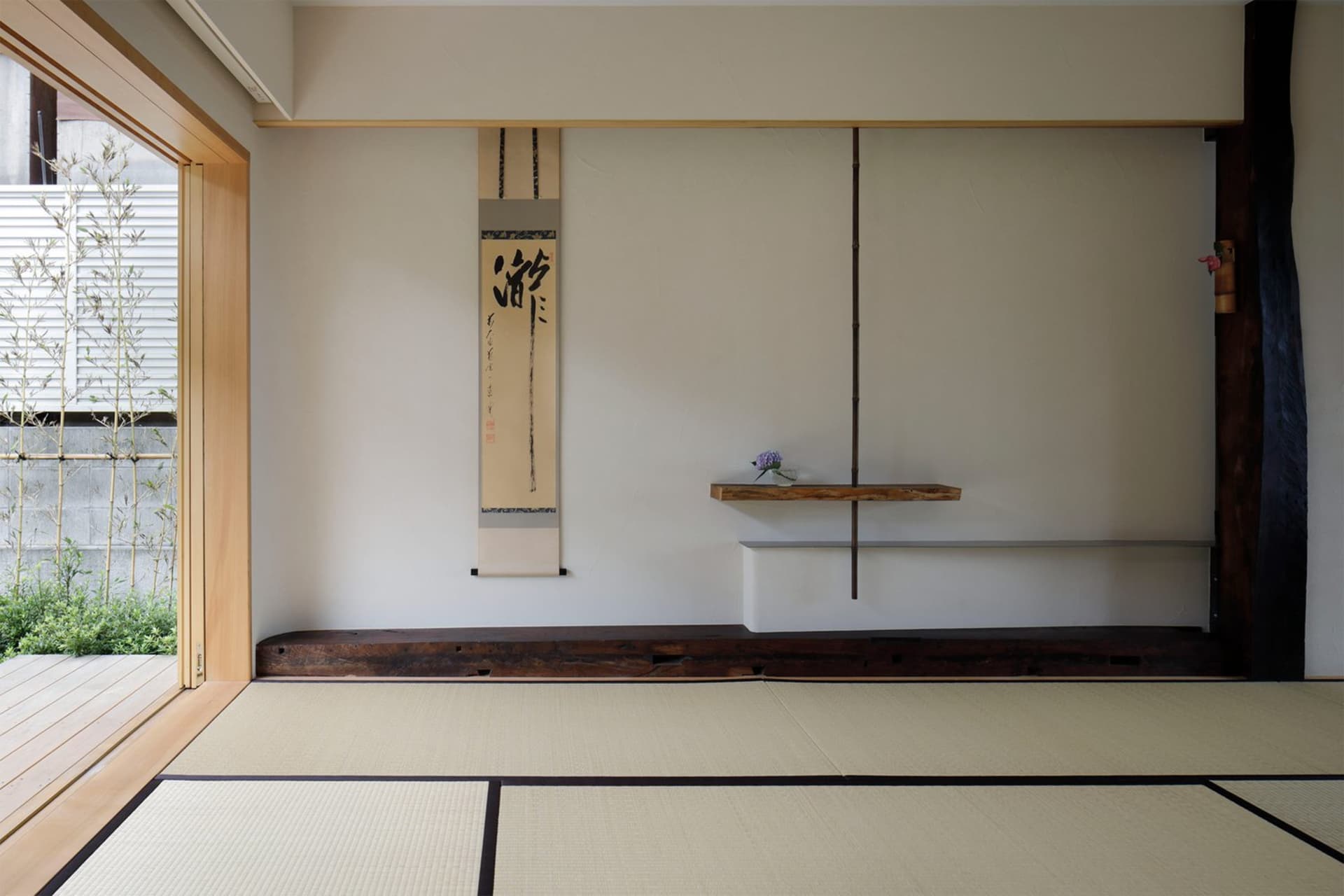 A minimalist living room with a wooden floor and tatami mats, featuring a simple yet elegant design with decorative plants an