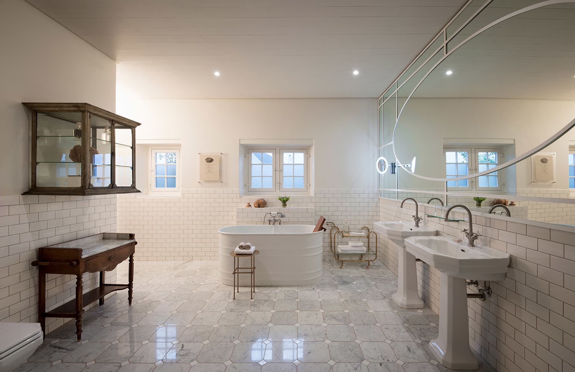 A modern bathroom with white tiles, marble floors, and a large white bathtub.