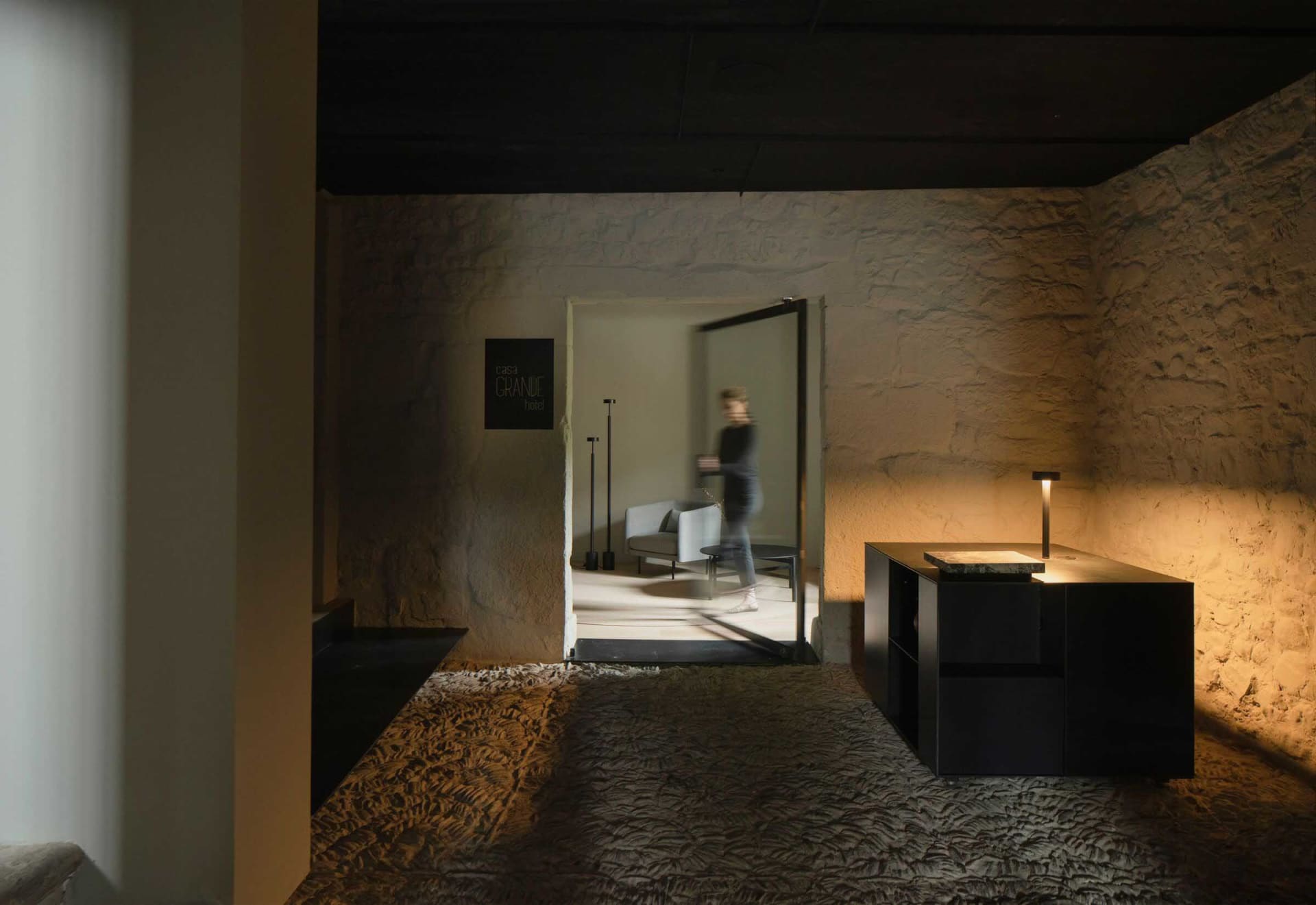 A minimalist hotel lobby with a modern design featuring concrete walls and floors, and sleek furniture.