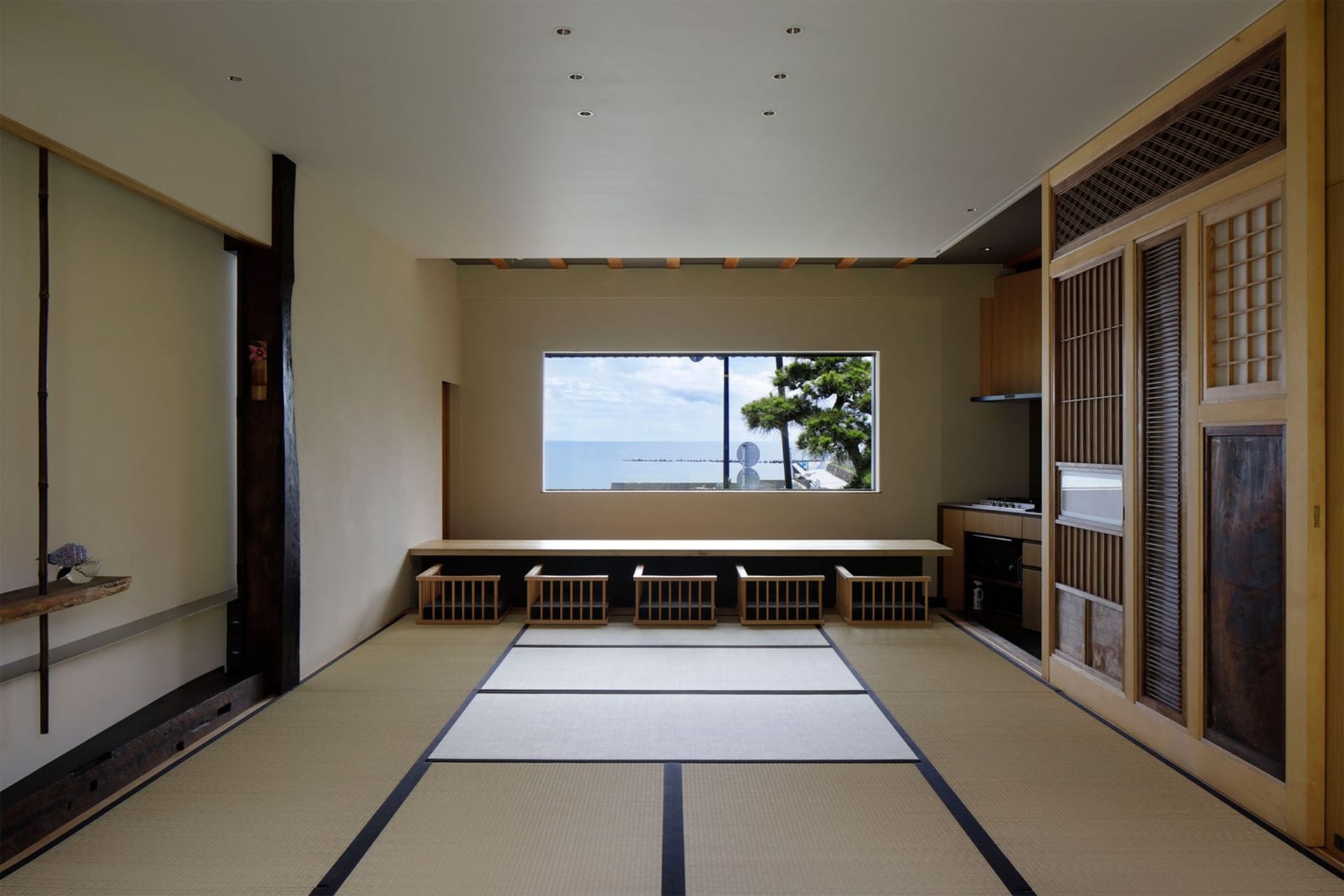 A modern living room with a natural fiber rug, featuring minimalist furniture and large windows overlooking the sea.