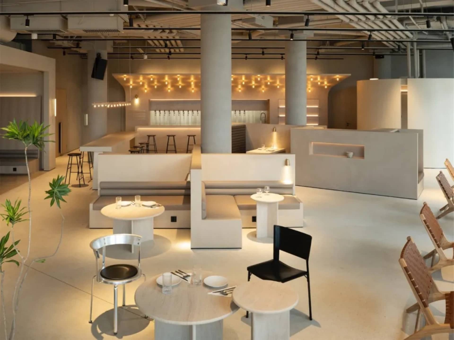 Modern minimalist restaurant interior with concrete pillars, wood benches, and round tables.