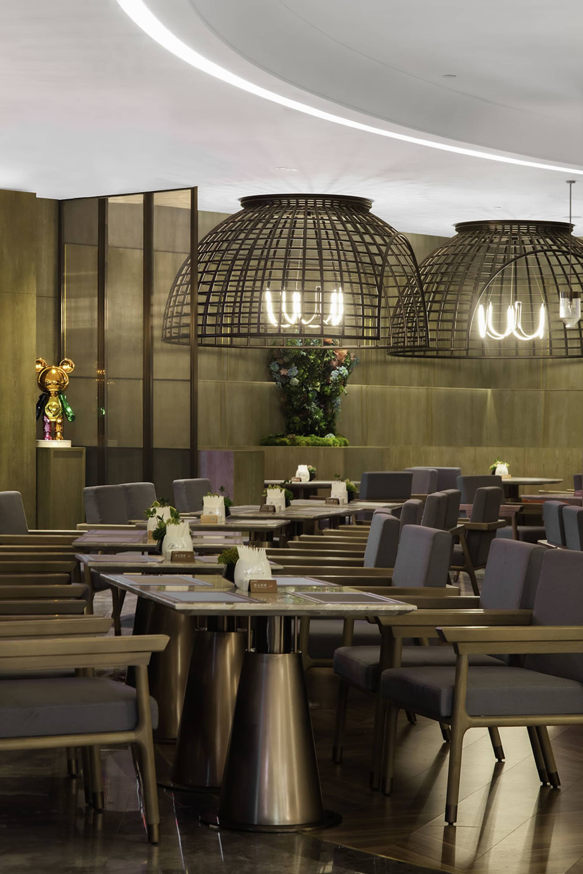 A modern restaurant interior with metal pendant lights, wooden tables, and glass panels.