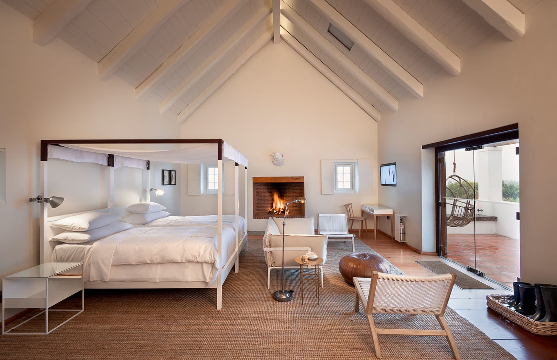 A minimalist bedroom with a white canopy bed, a fireplace, and a hanging chair outside.