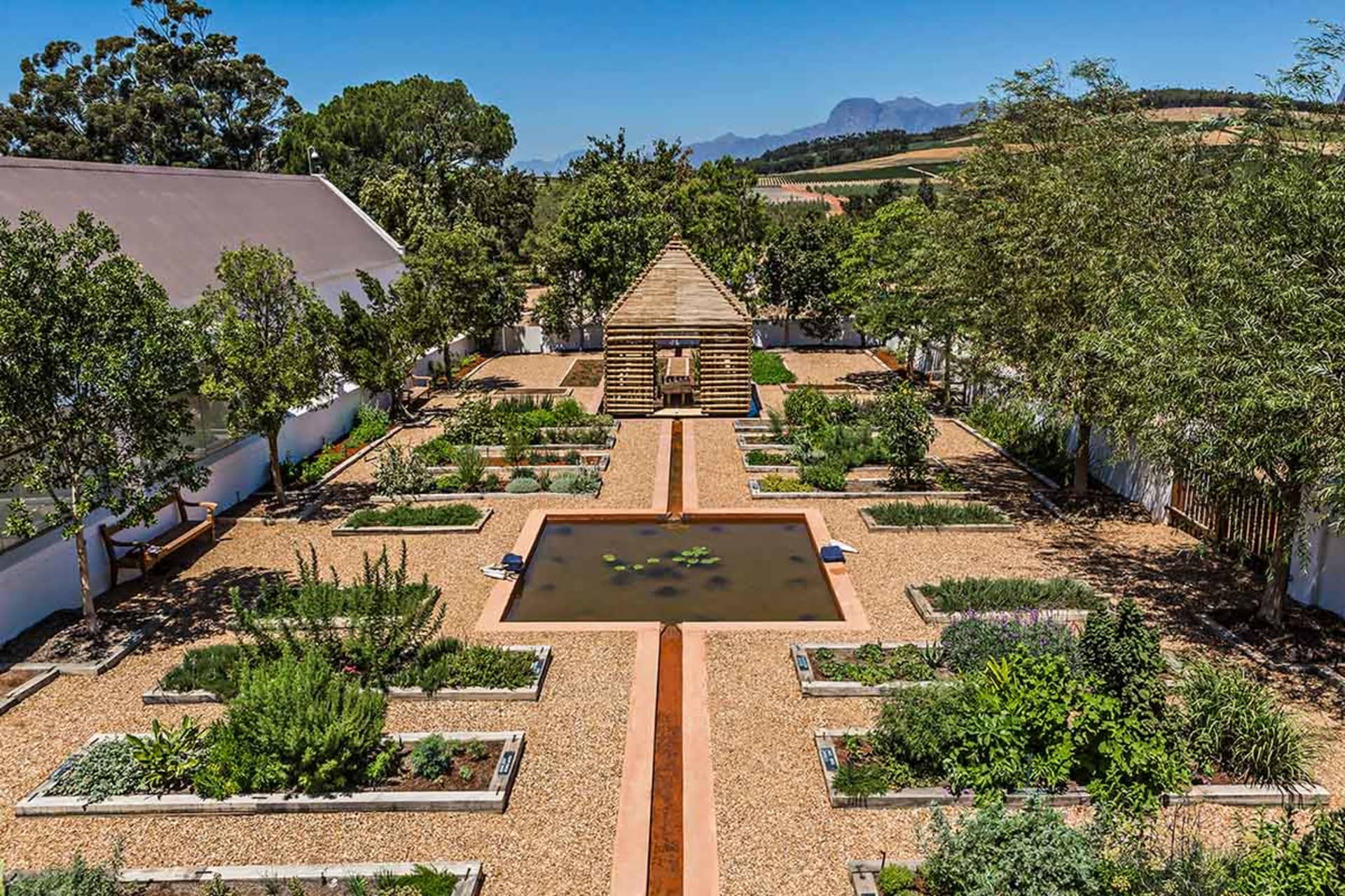 A modern garden featuring natural materials and a water feature surrounded by raised beds.