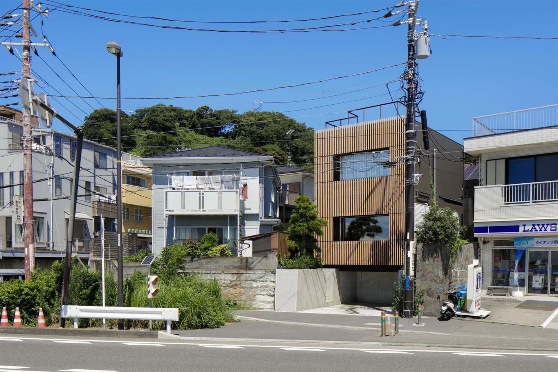 一棟現代建築採用木質板材、混凝土與玻璃立面,坐落於有電線與路燈的街道上。
