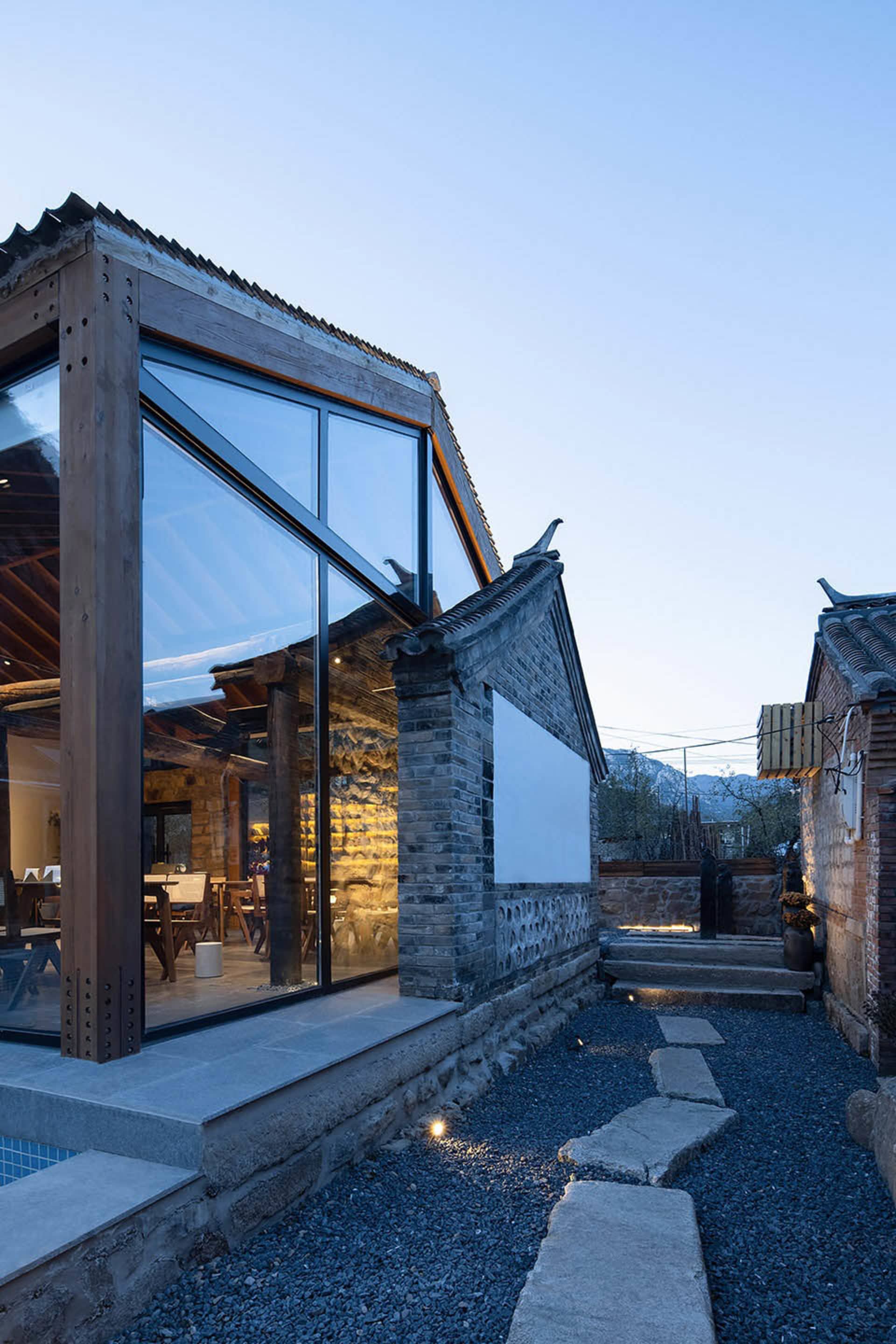 An outdoor view of a modern residential exterior featuring stone, glass, and wood materials under a clear sky.