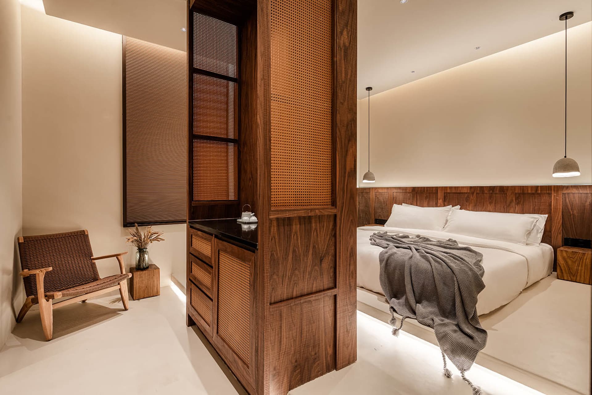 A minimalist bedroom featuring white walls and a wooden bed frame with a grey blanket draped over it.