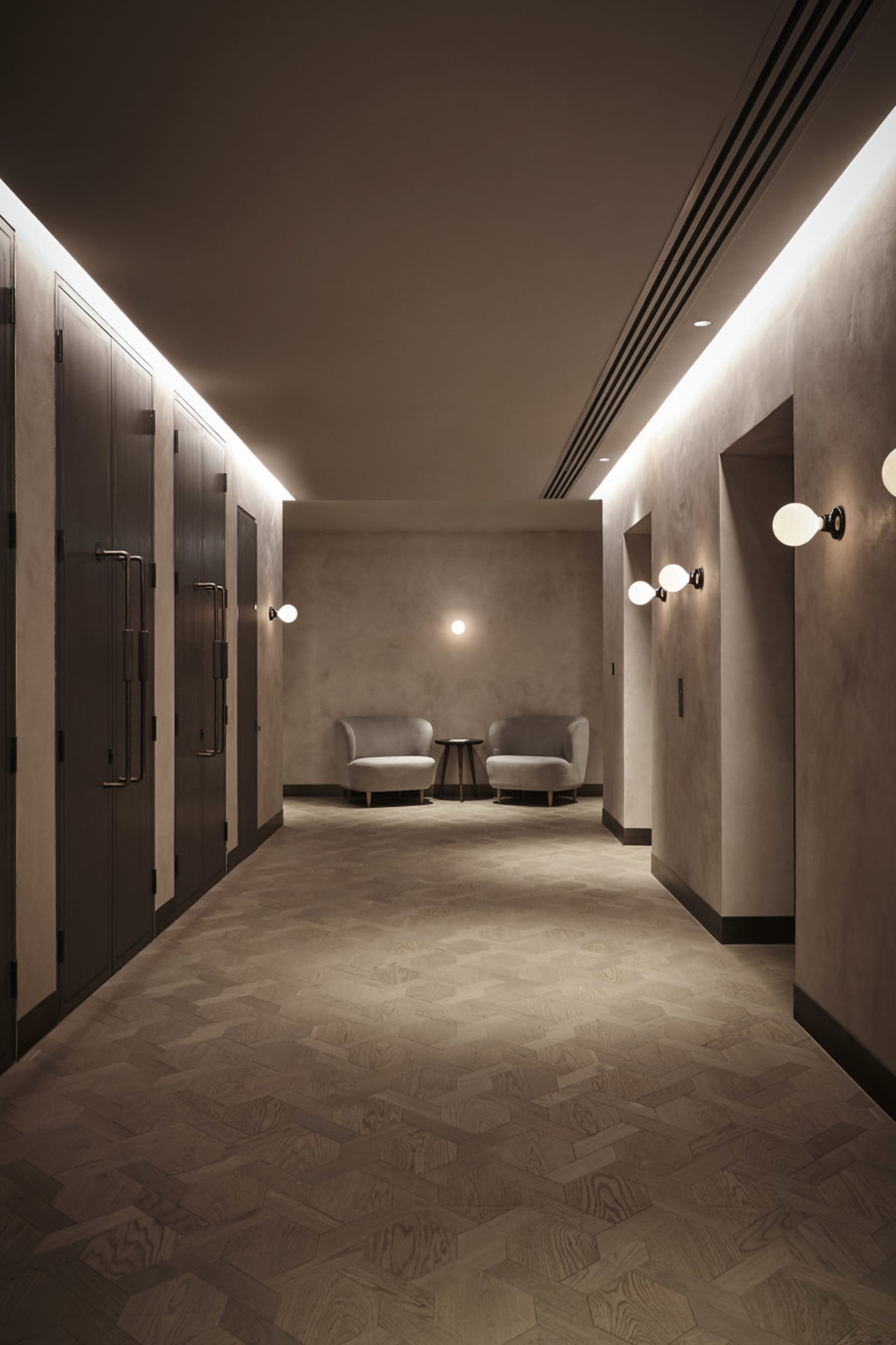 A minimalist corridor with wooden flooring and walls, featuring two armchairs.
