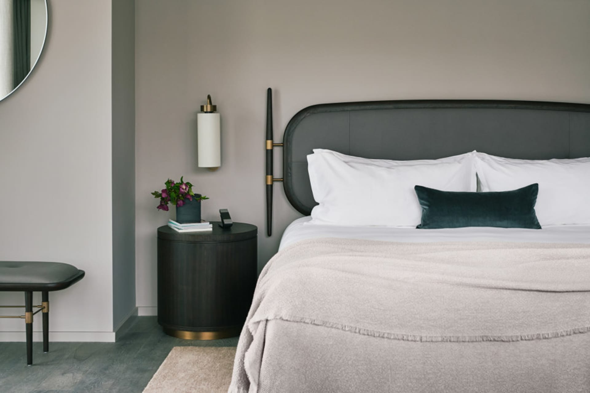 A modern bedroom featuring a fabric bed with a black headboard on a grey floor, accompanied by a side table with a lamp and a