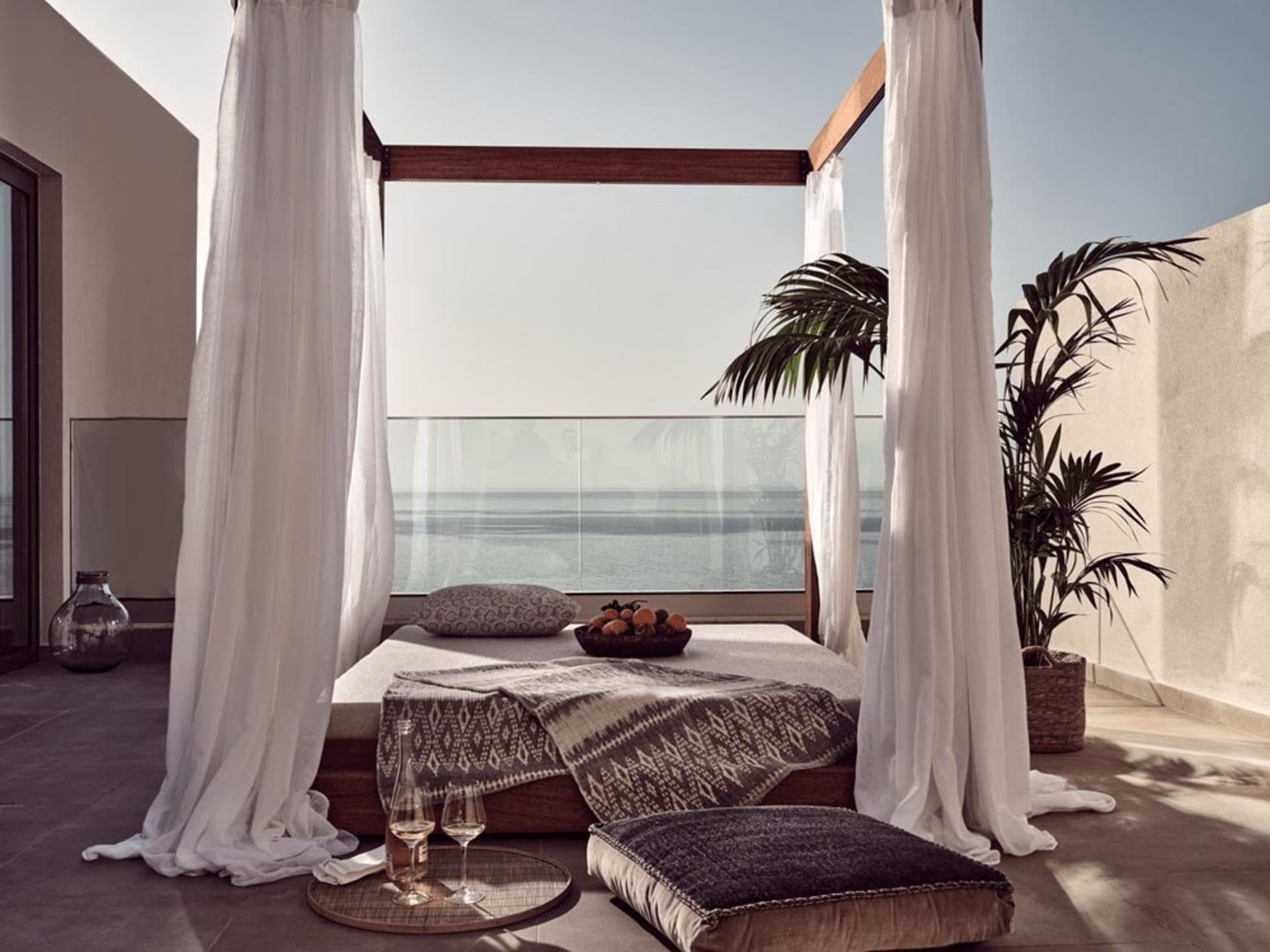 A modern bedroom featuring a bed with a canopy, white curtains, and a view of the ocean.