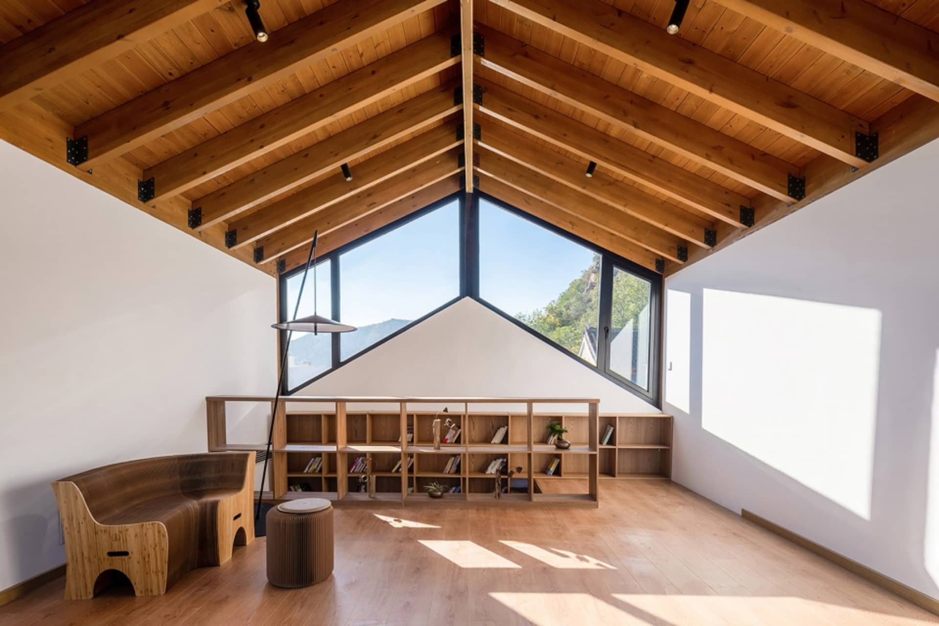 A modern living room with a high ceiling, wooden shelves, and a view of the outdoors.