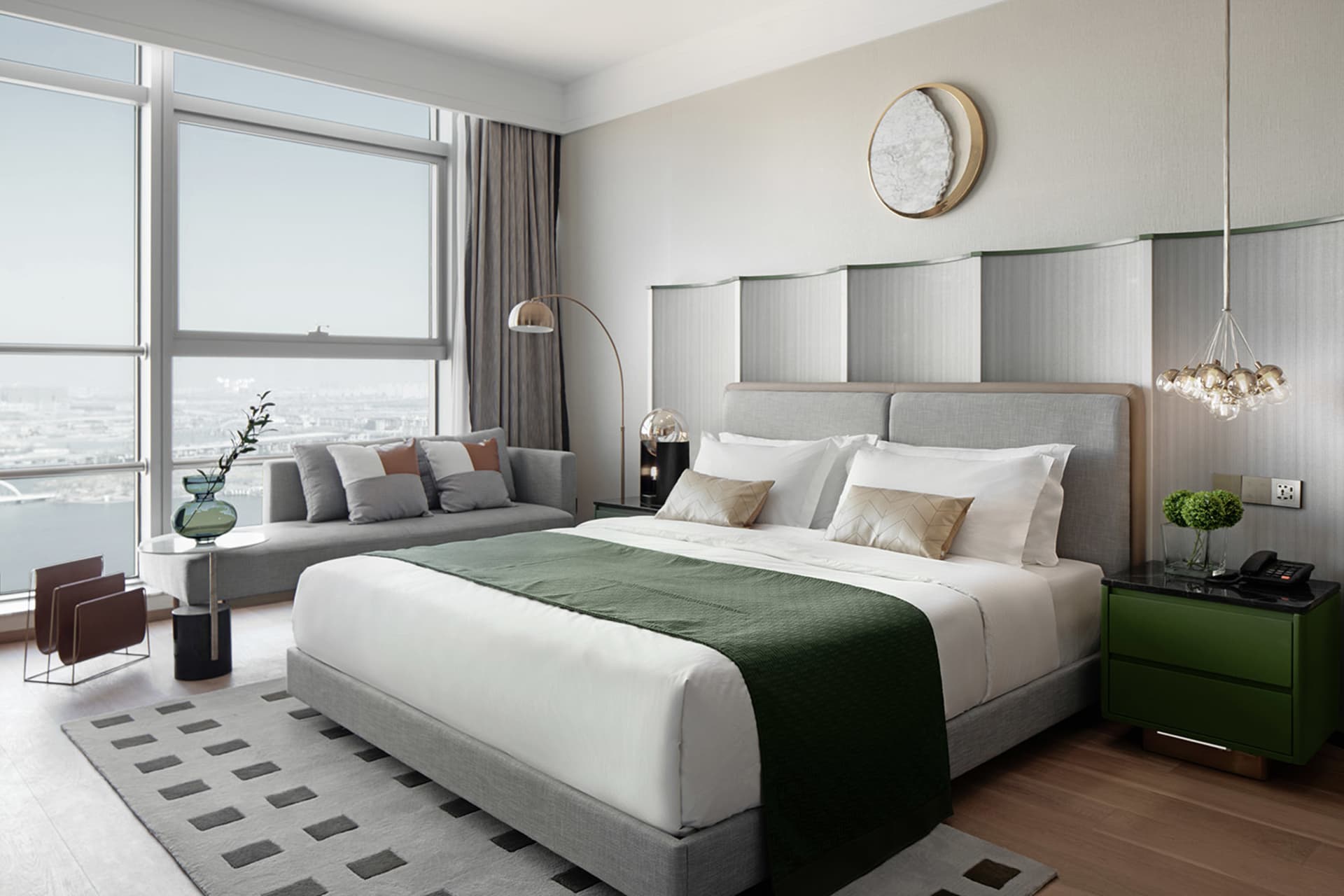 A modern minimalist bedroom with a gray bed, white linens, and a green throw blanket.