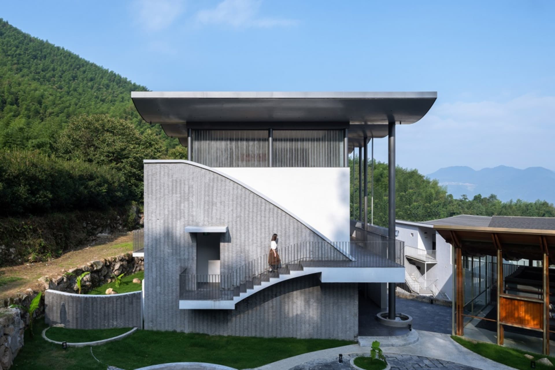 Modern residential exterior with concrete walls, matte black metal accents, terraces, and balconies overlooking greenery and