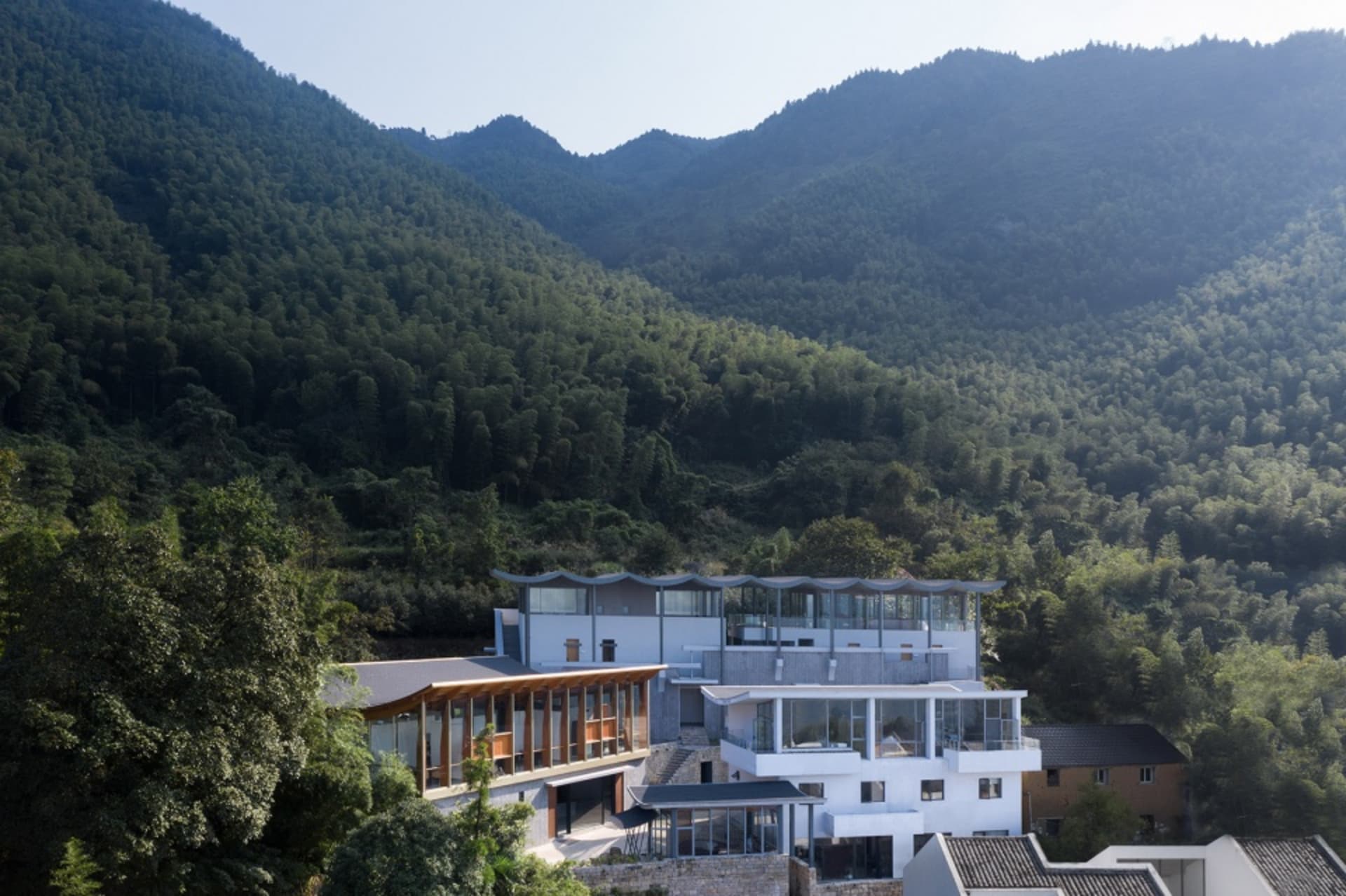 Modern house with glass walls overlooking green hills and mountains.