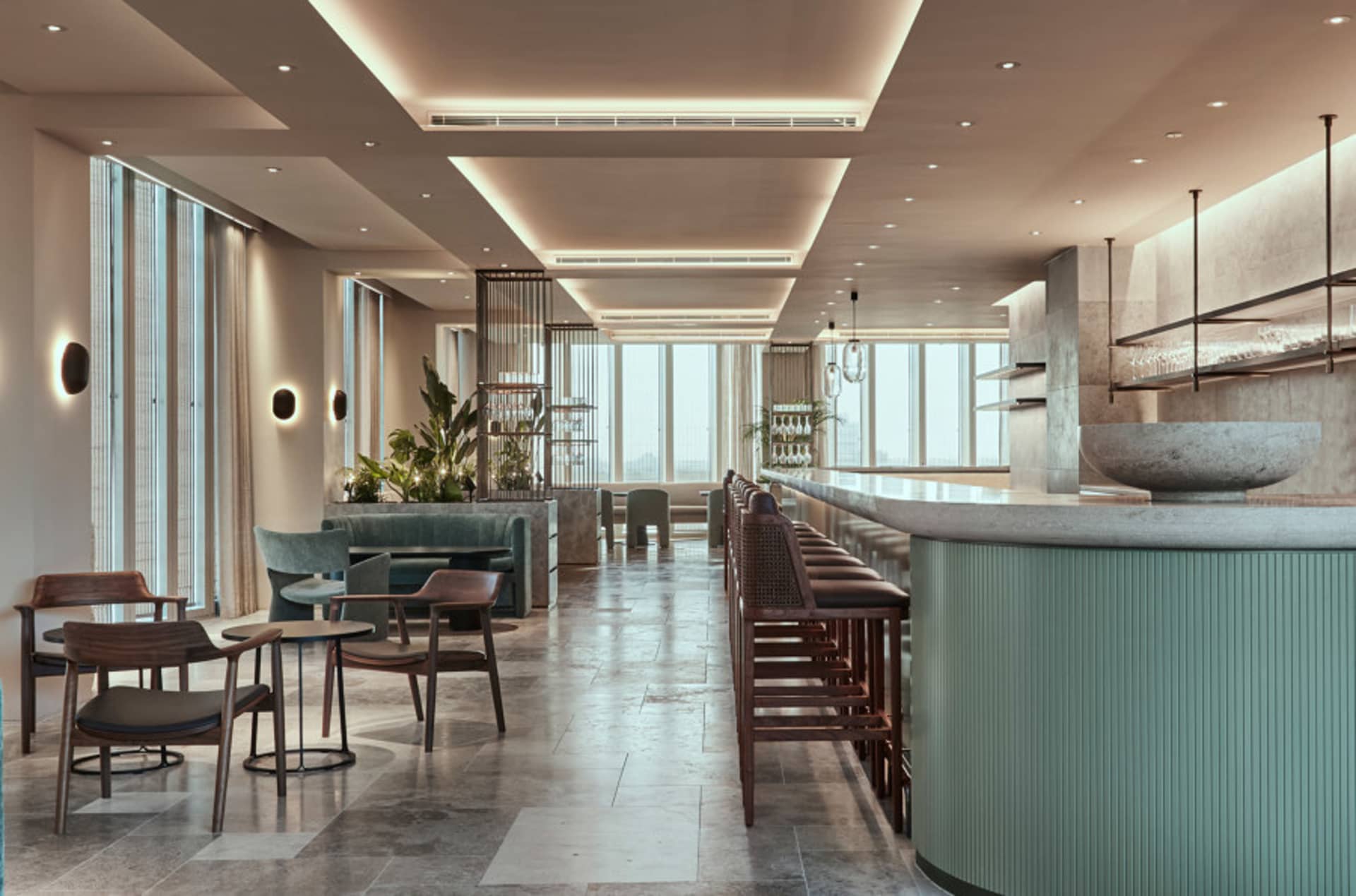 A modern restaurant bar with concrete and glass elements and green plants.