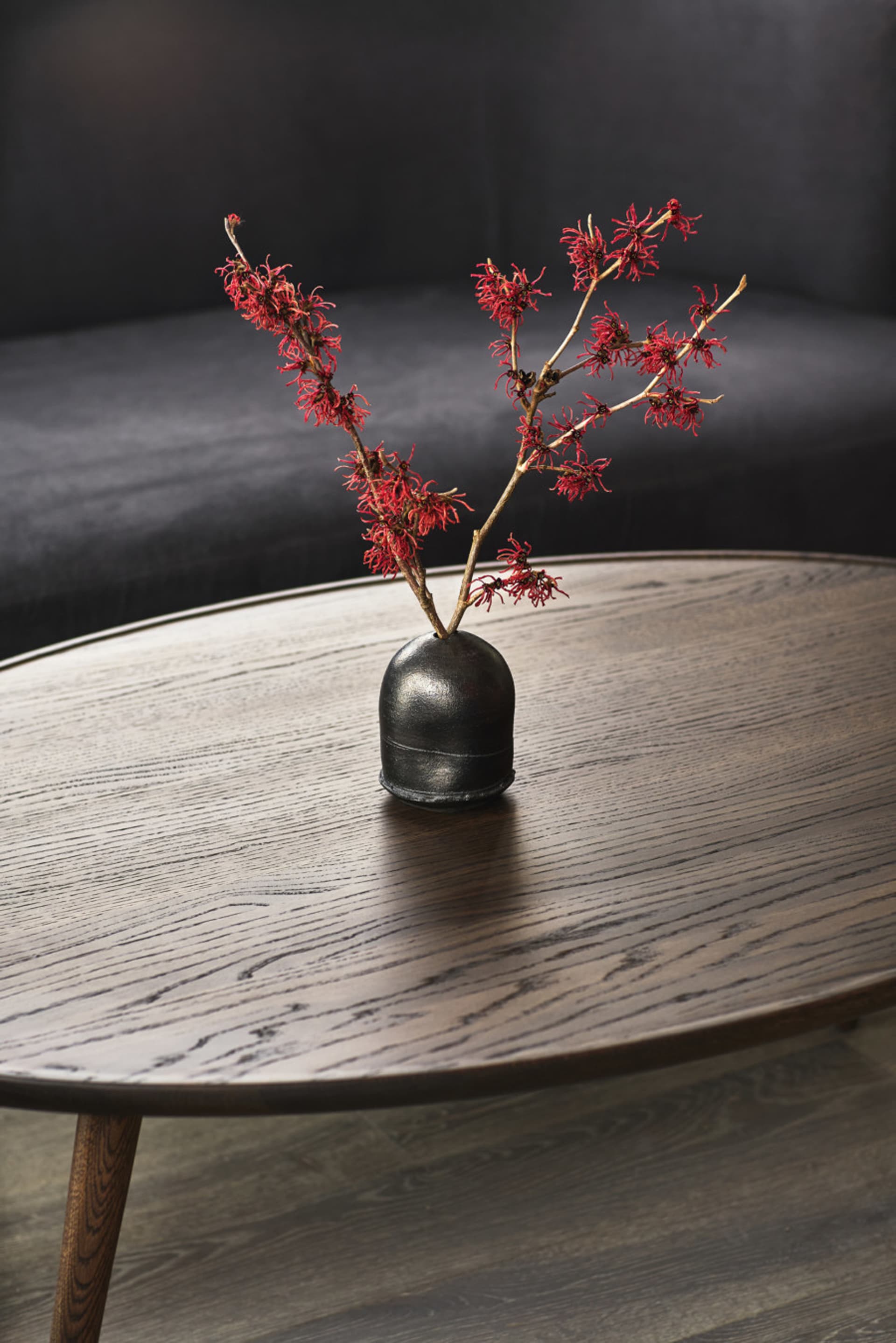 A close-up of a wooden coffee table featuring a black vase with a decorative branch arrangement.