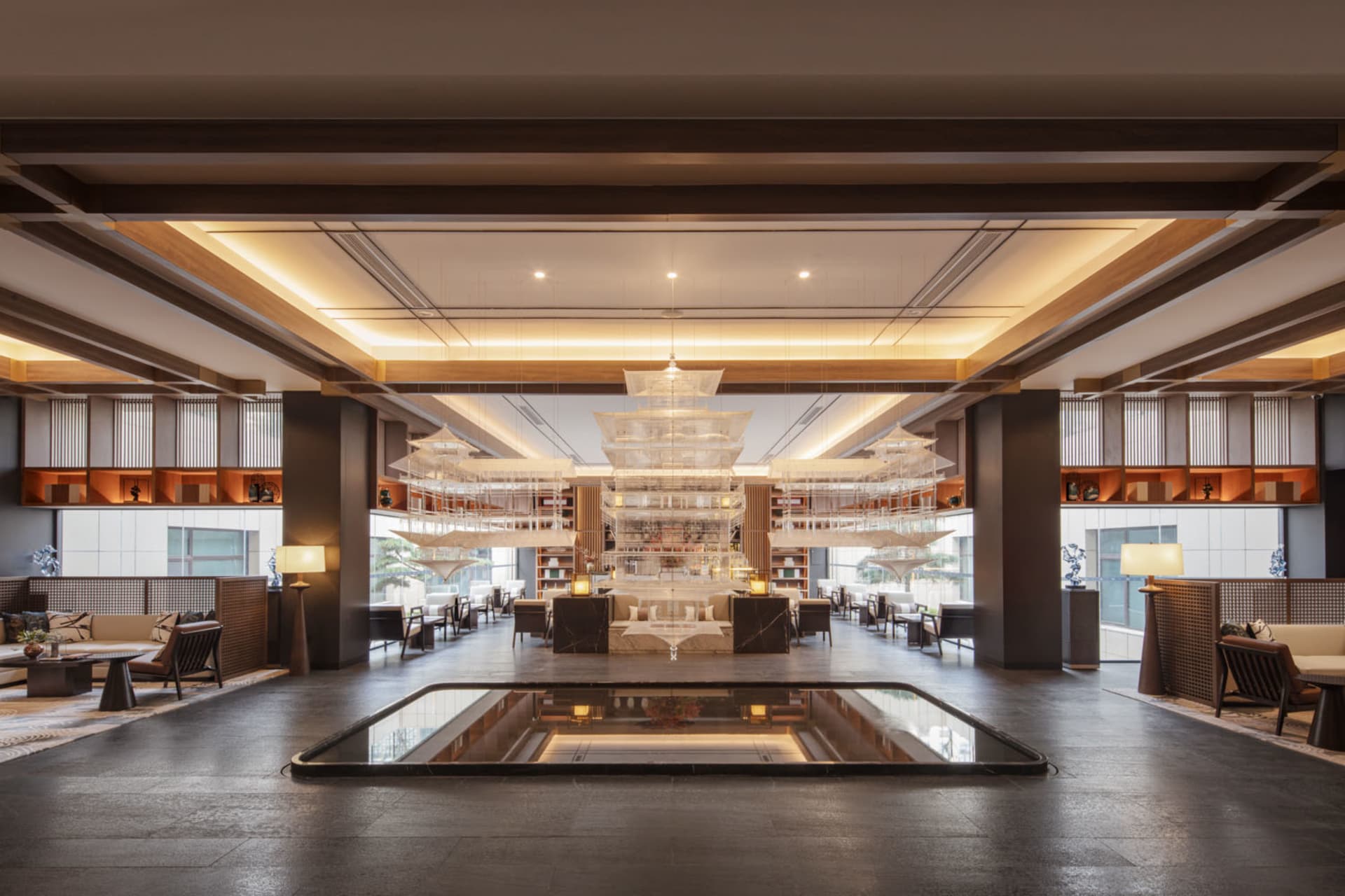 A modern hotel lobby with marble flooring, wooden beams, and a central water feature.