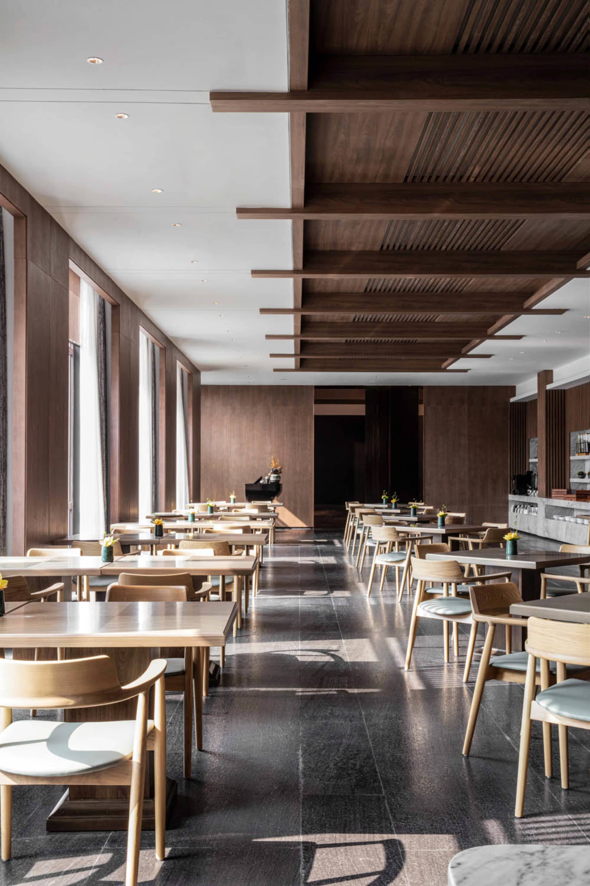 Modern restaurant interior with wooden tables, chairs, and marble accents.