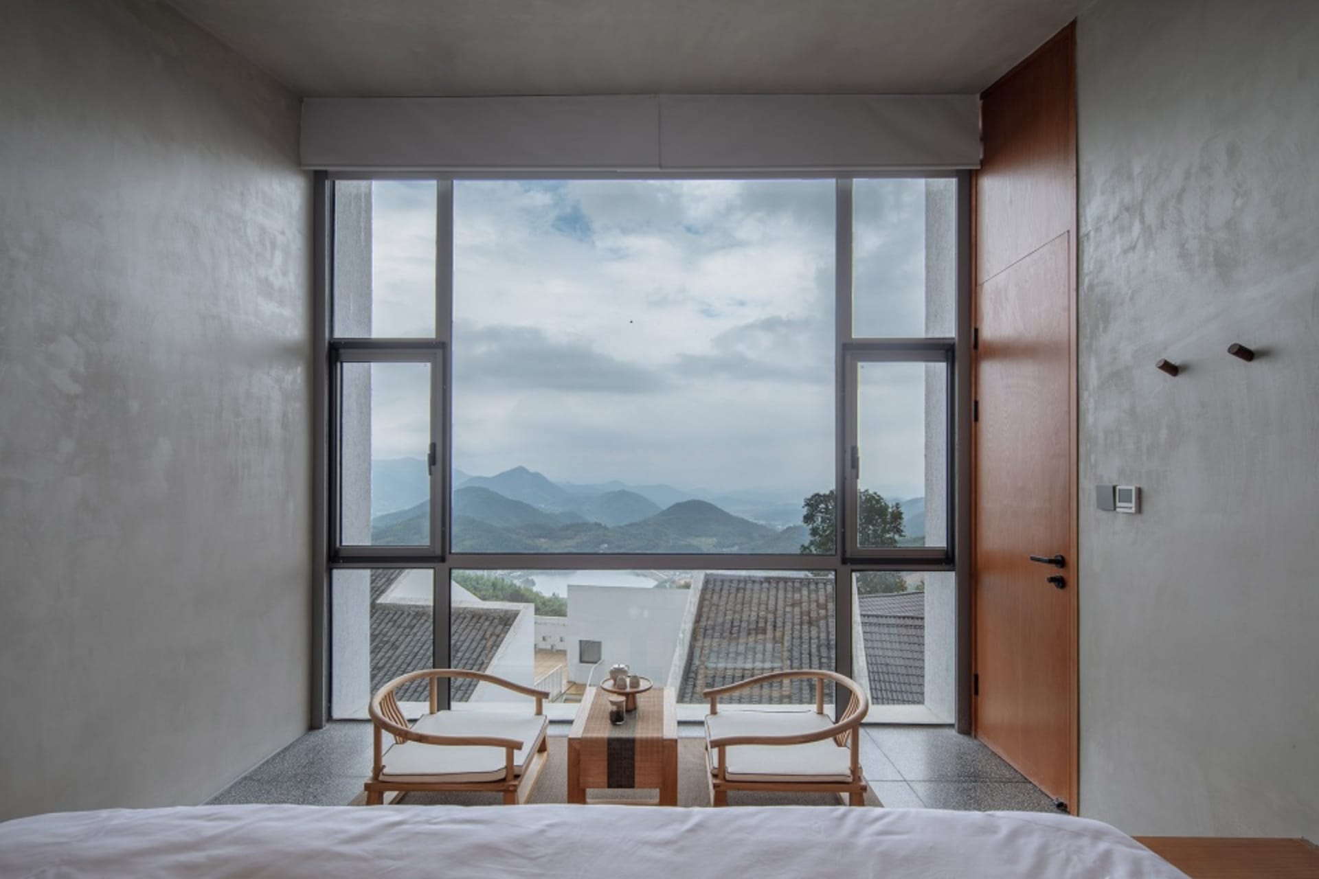 Modern bedroom with large glass window displaying scenic mountain views.