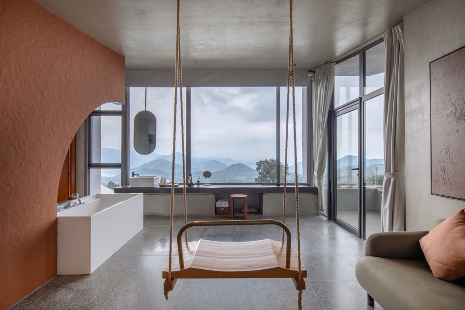 Modern living room featuring a wood swing hanging from the ceiling, a large window with a view of the mountains, and a sofa w