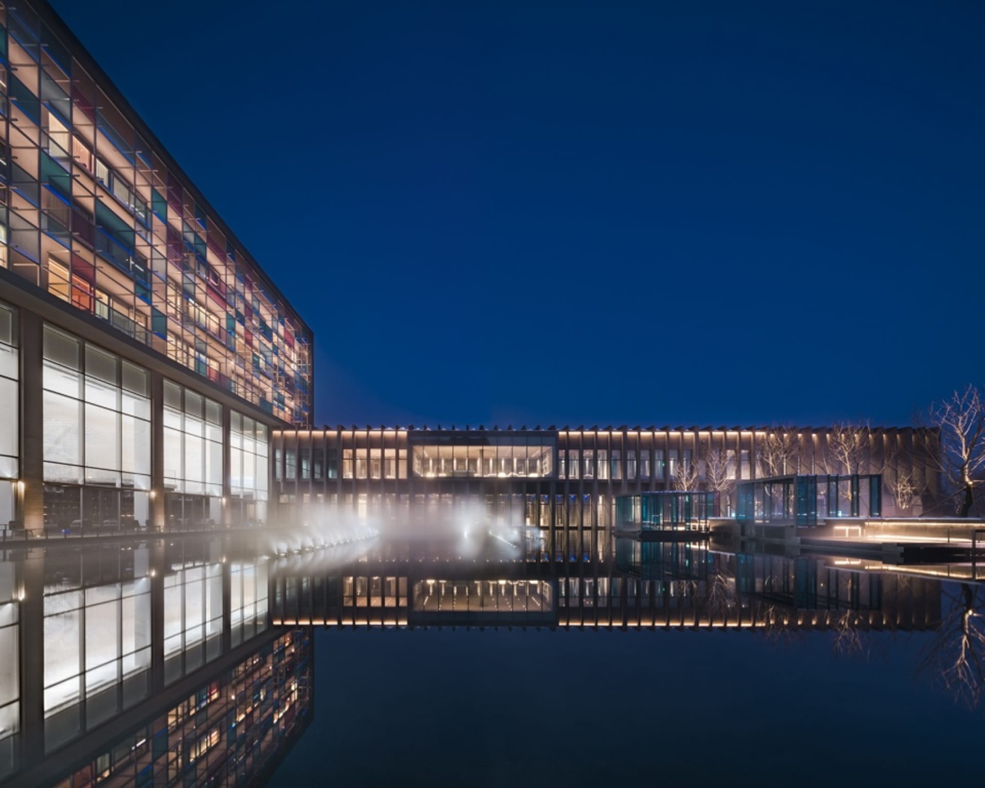Modern building with glass walls and steel accents reflecting in a calm water feature