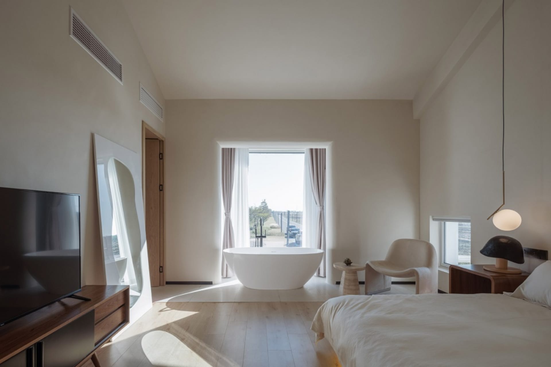 Modern minimalist bedroom featuring a concrete bathtub, wood flooring, and glass windows.