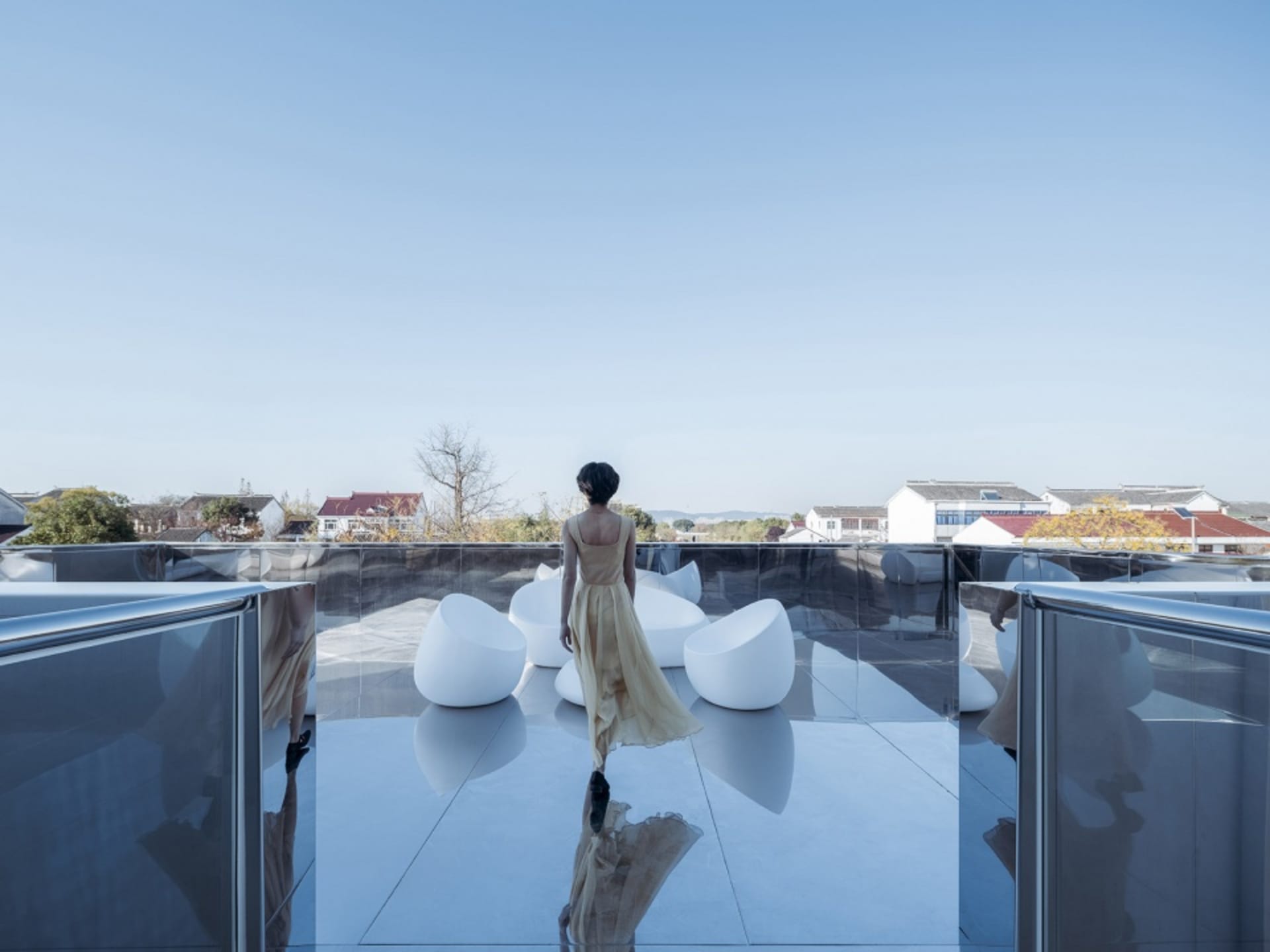 A modern rooftop space featuring glass furniture and a single individual.
