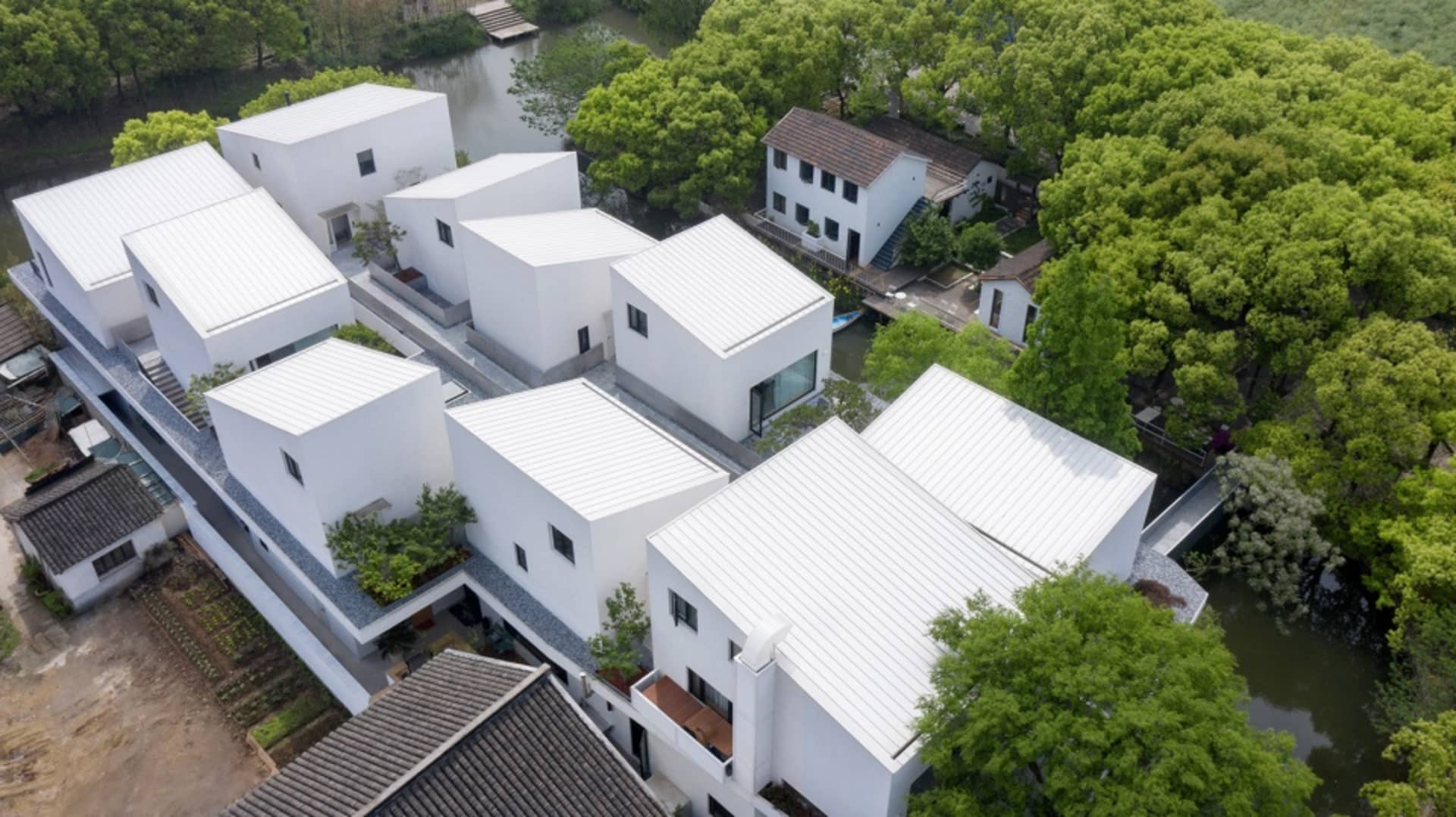 Aerial view of modern residential architecture with white metal roofing surrounded by green trees and water channels.