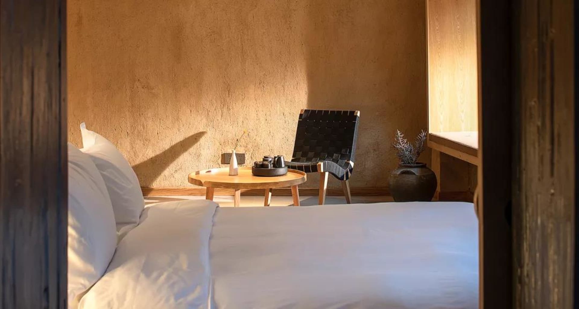 A minimalist bedroom with a white bed, wooden furniture, and a woven chair.
