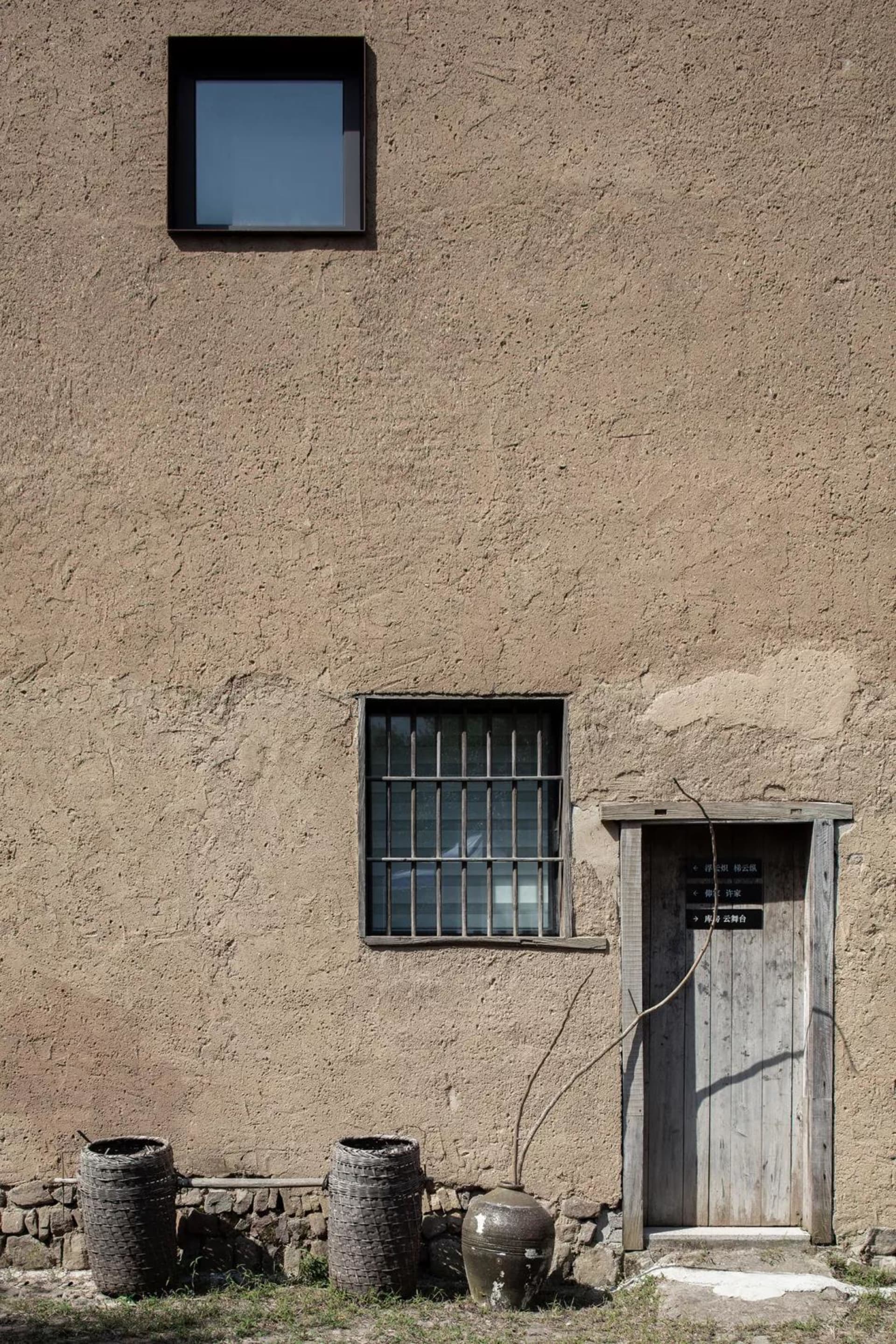An old residential entry with a wooden door and two barred windows on a textured stucco wall.