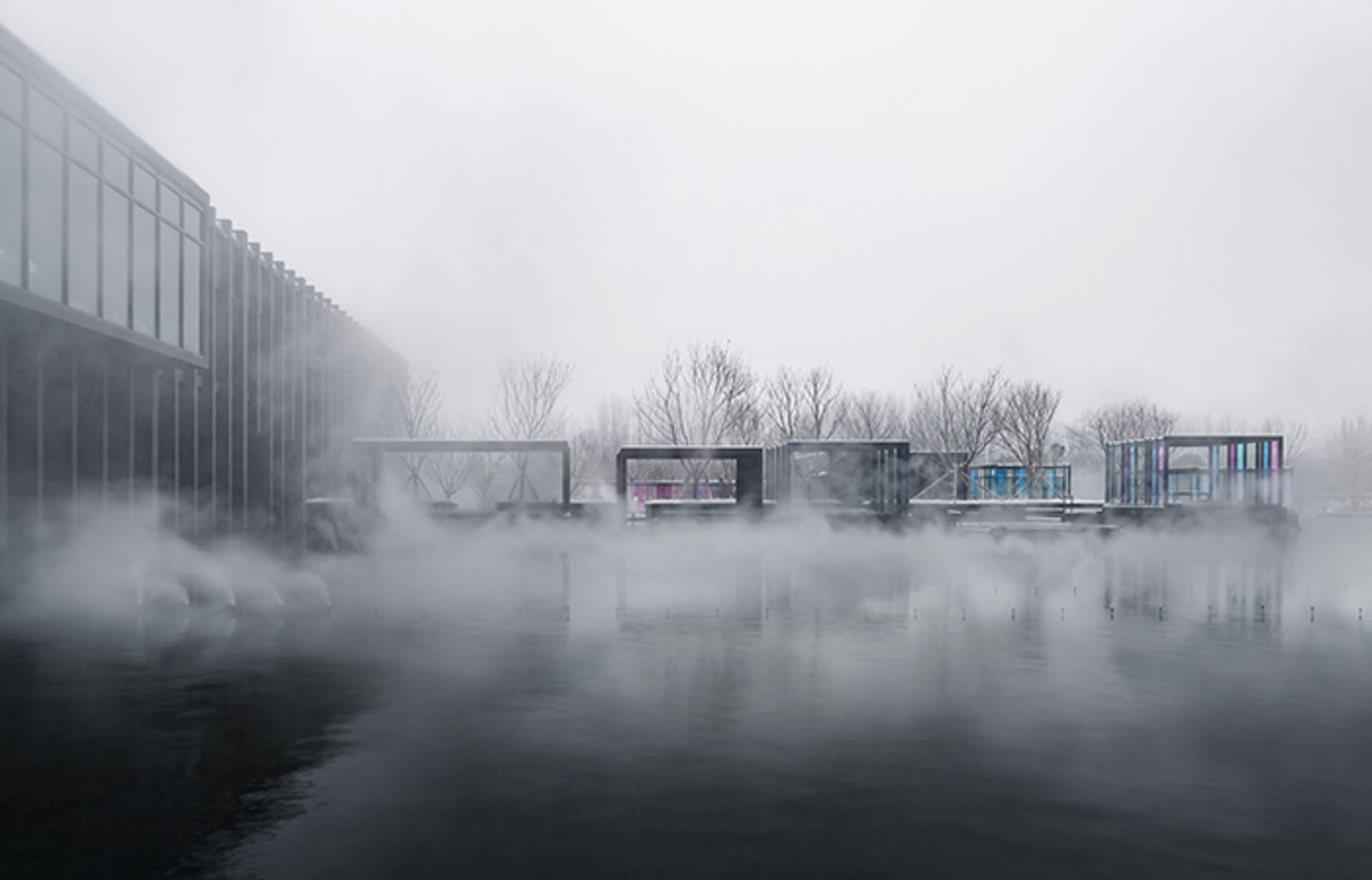 Minimalist architectural design featuring glass and concrete structures by a foggy water body.