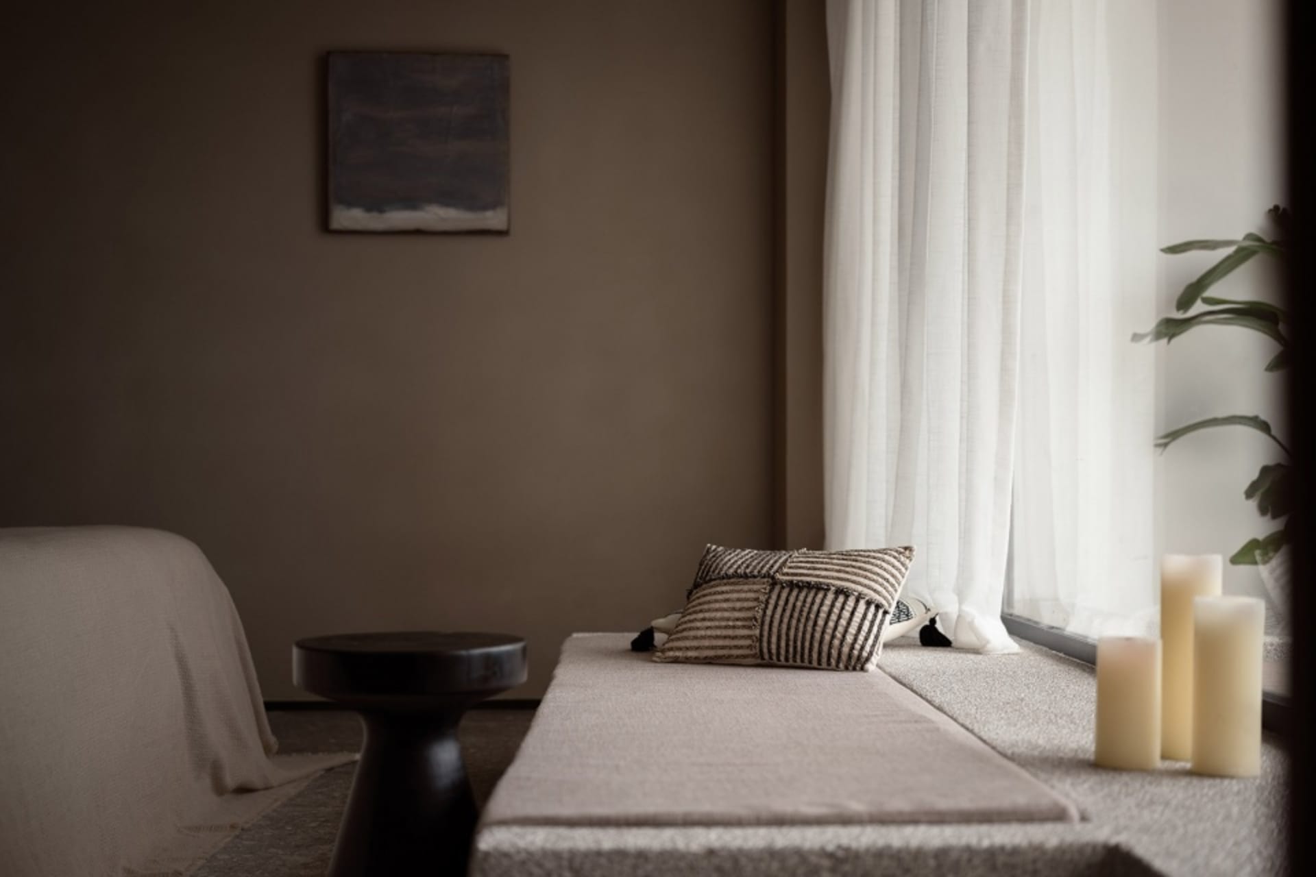A minimalist bedroom featuring textured textiles on a window seat and a black stool.