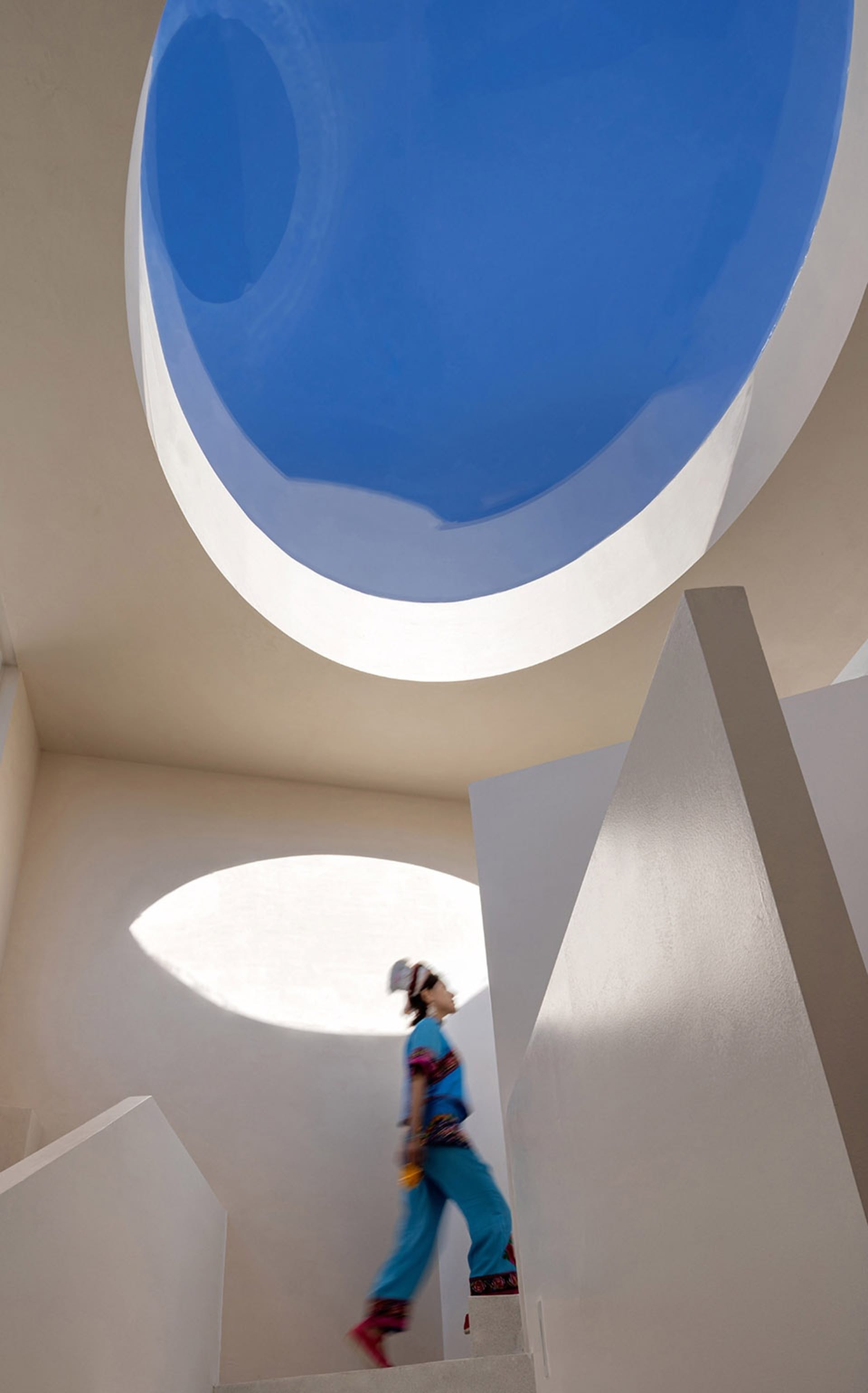 A modern architectural space with a concrete floor and walls, featuring a large circular opening in the ceiling.