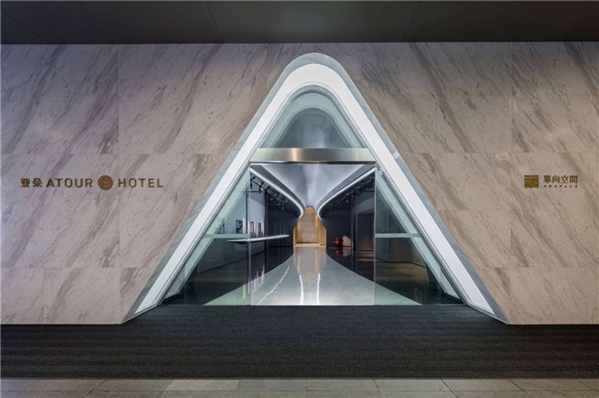 Modern hotel entrance featuring marble walls, glass doors, and metallic accents.