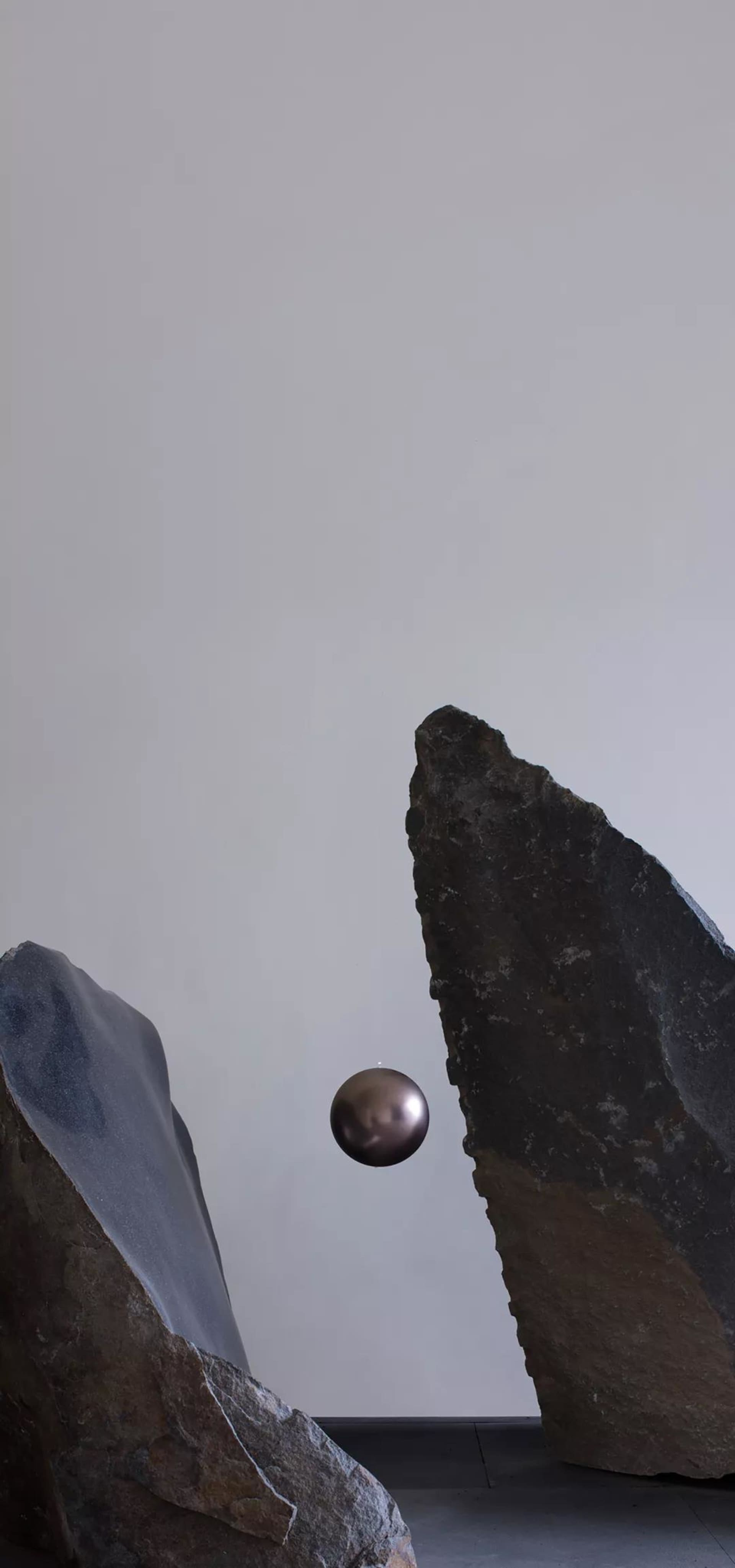 一個金屬球懸浮在兩塊不規則岩石造型之間,背景為純白。
